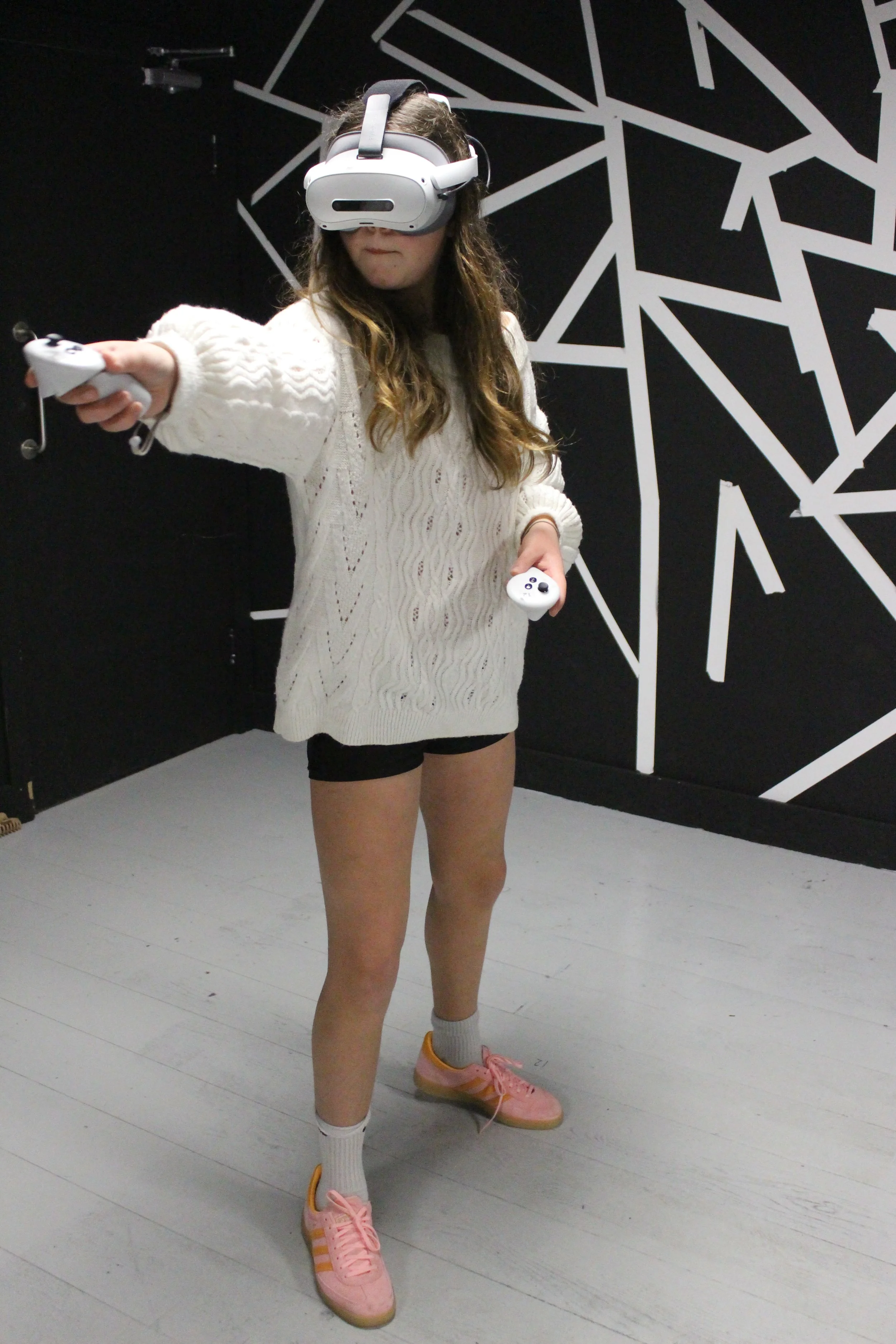A woman wearing a virtual reality headset and holding a controller, standing in a room with abstract black and white wall art.
