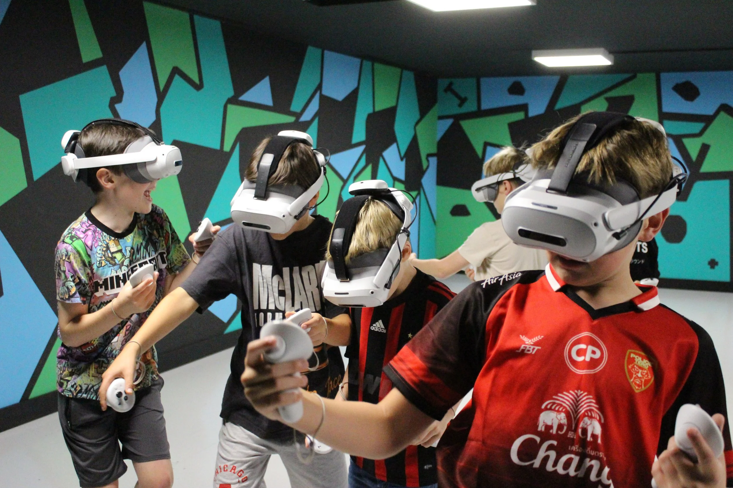 Group of young boys wearing virtual reality headsets and holding controllers in a modern room with a colorful geometric mural on the wall.