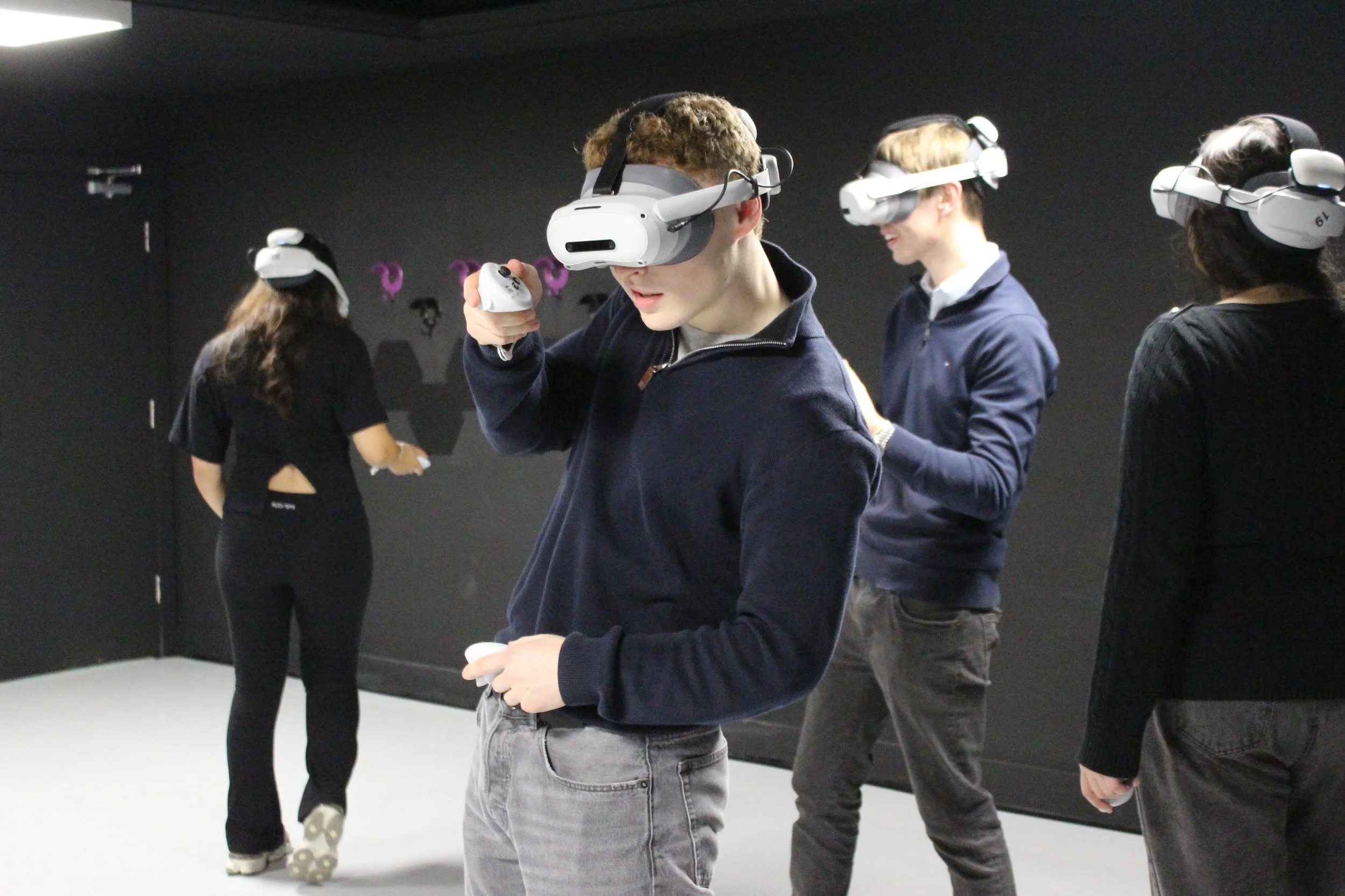 Group of young adults wearing virtual reality headsets in a dark indoor space, engaging with VR experiences.