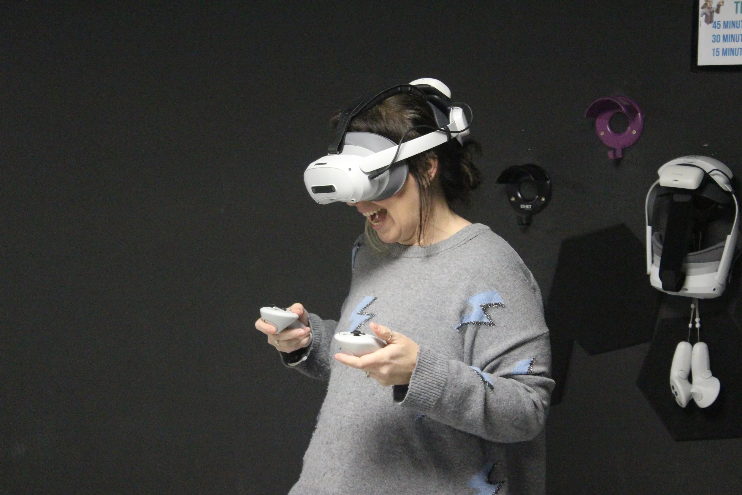 A woman wearing a virtual reality headset and holding two controllers, smiling and laughing.