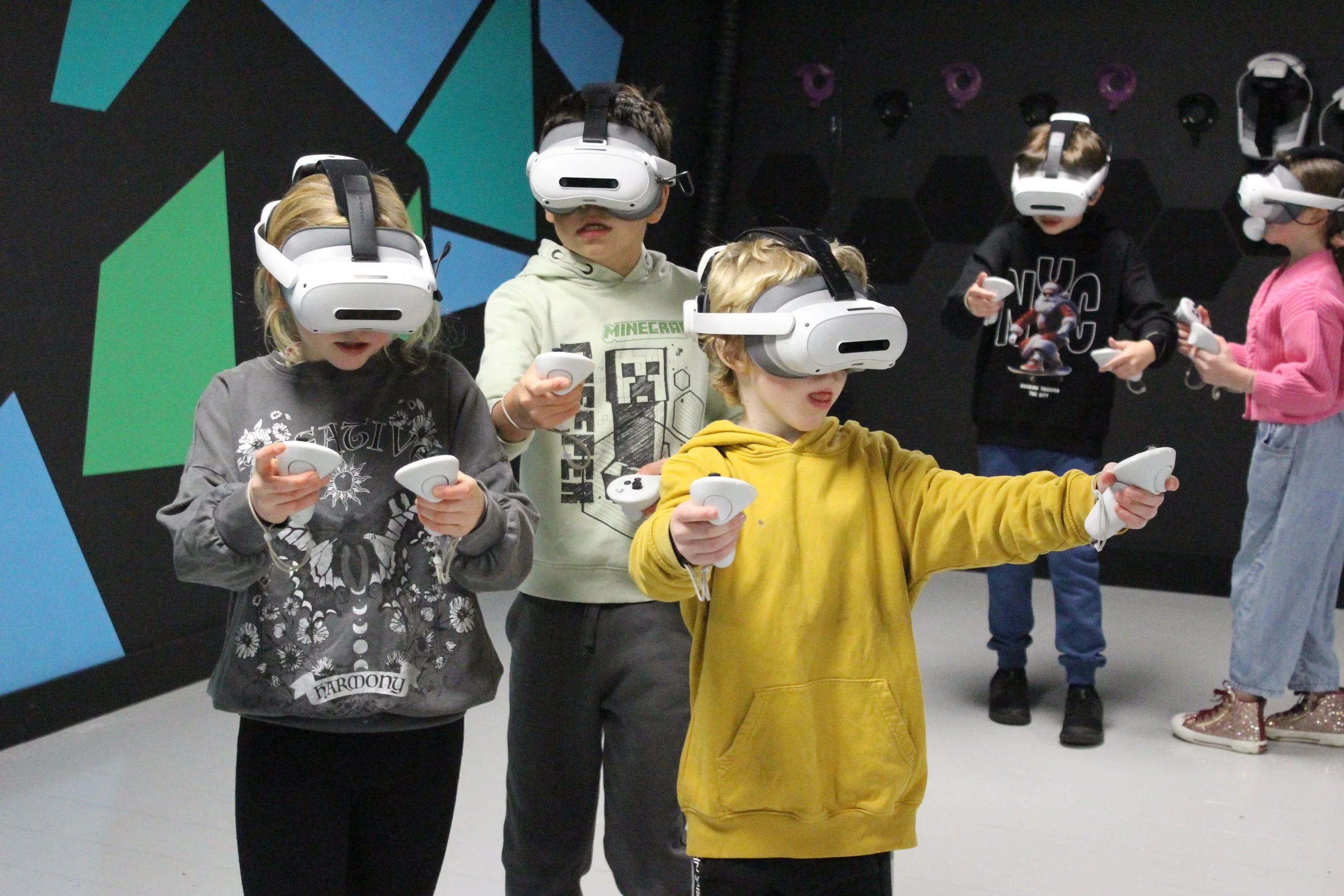 Group of children wearing virtual reality headsets and holding controllers in an indoor arcade or gaming center