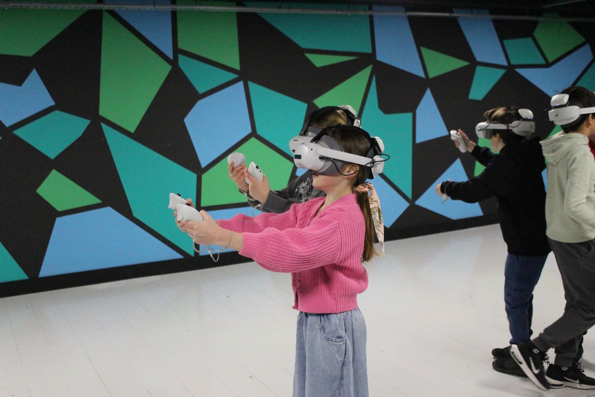 Children wearing virtual reality headsets in a room with a colorful geometric mural.