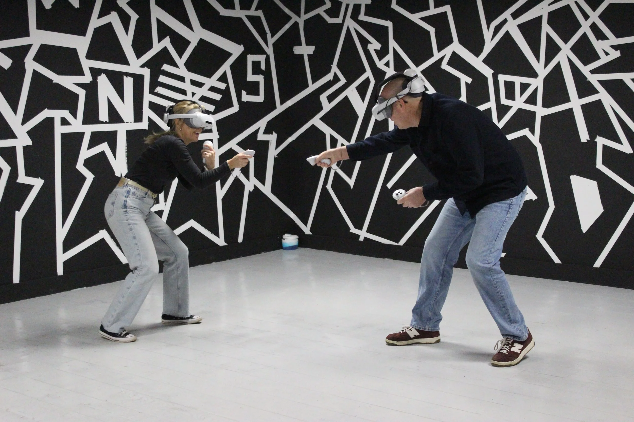 Two people wearing virtual reality headsets playing a game or engaging in an activity in a black and white striped room.