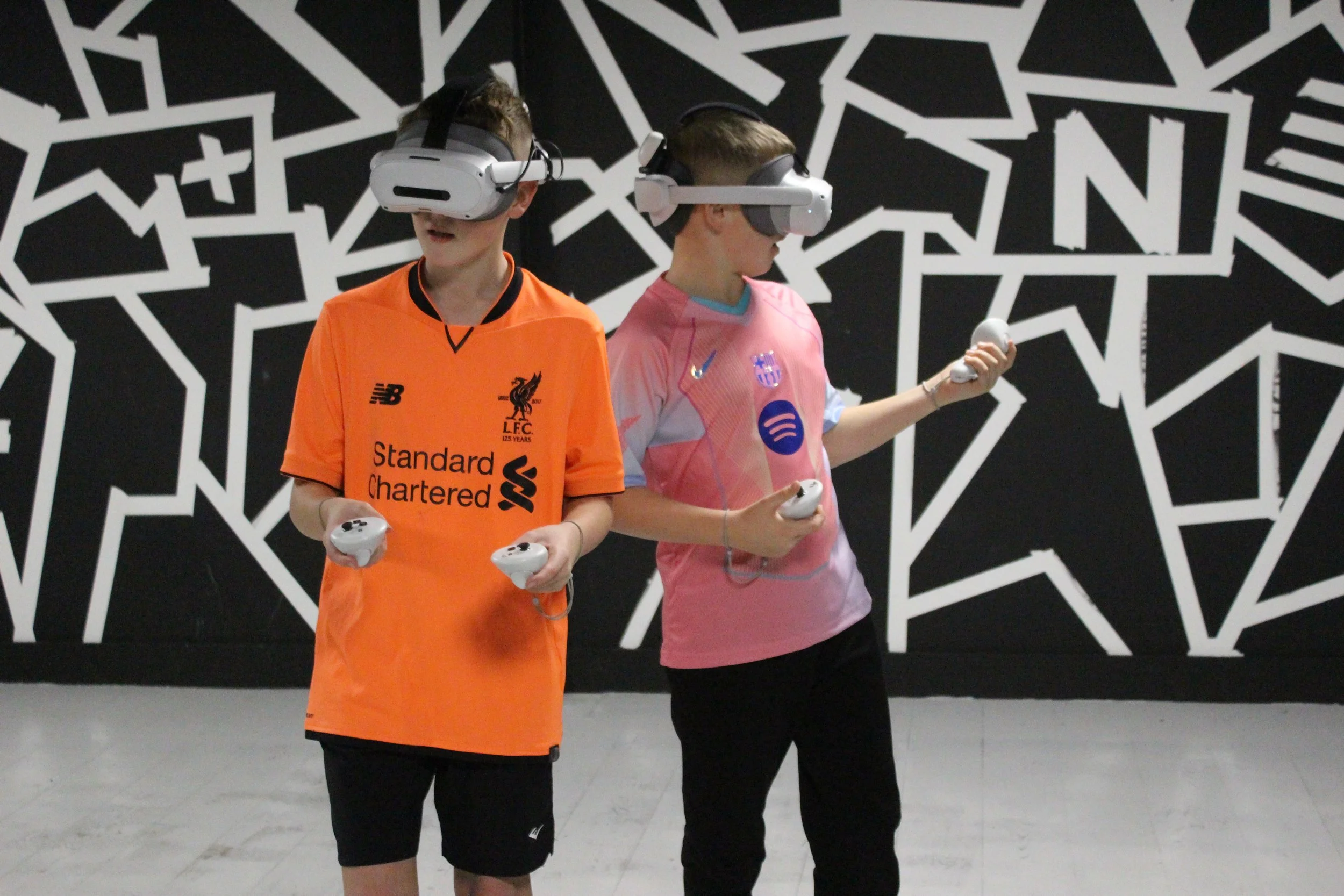 Two children wearing virtual reality headsets and holding controllers, standing in front of a black and white abstract background.