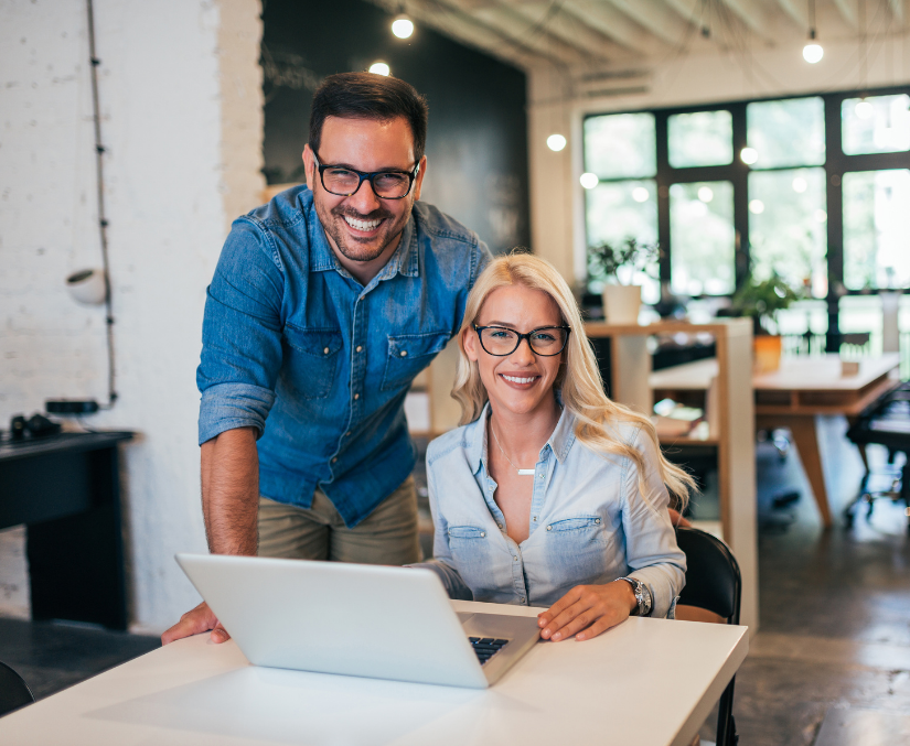 A man and woman smiling at a laptop in an office.