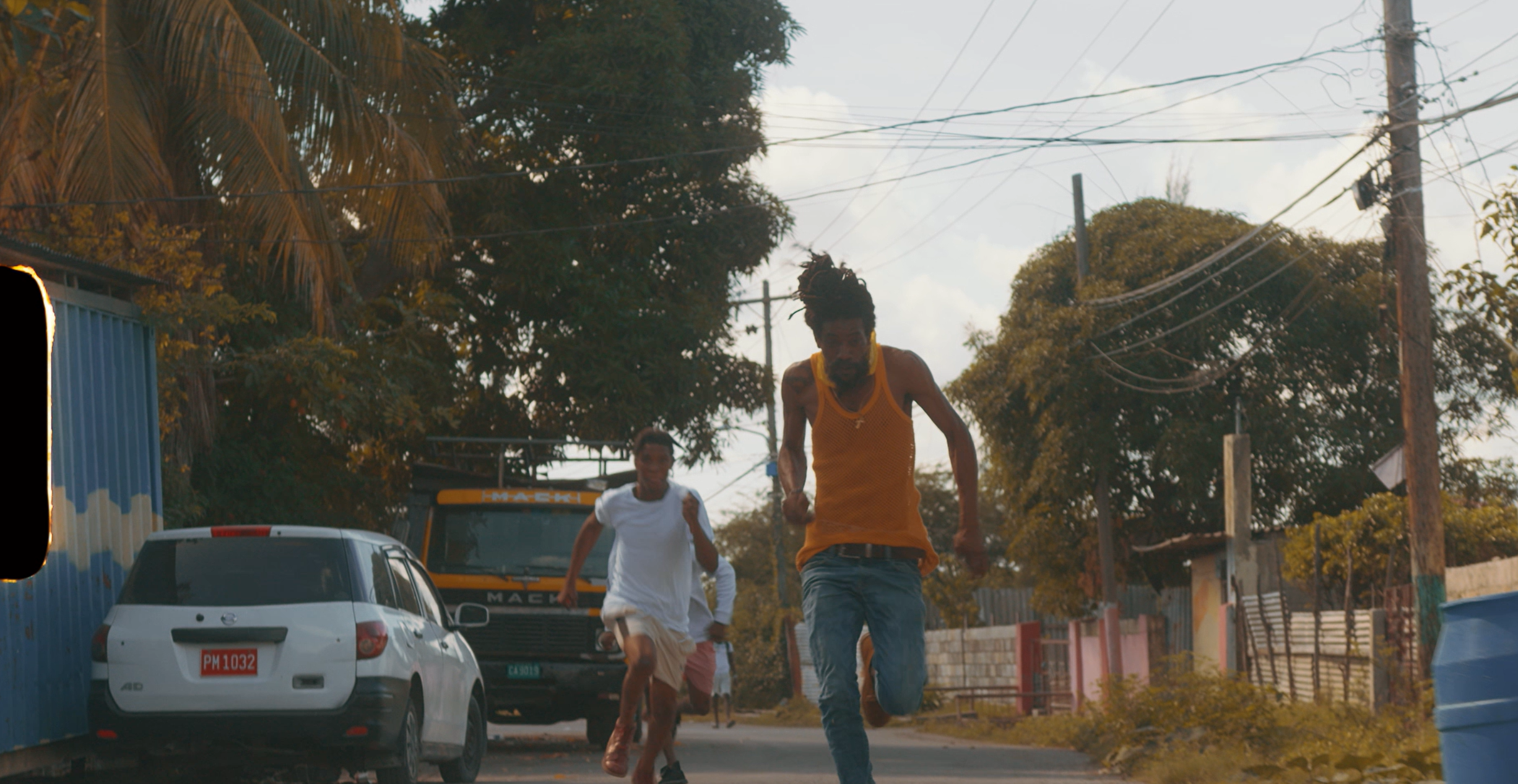 Three people running on a street, with cars and trees in the background.
