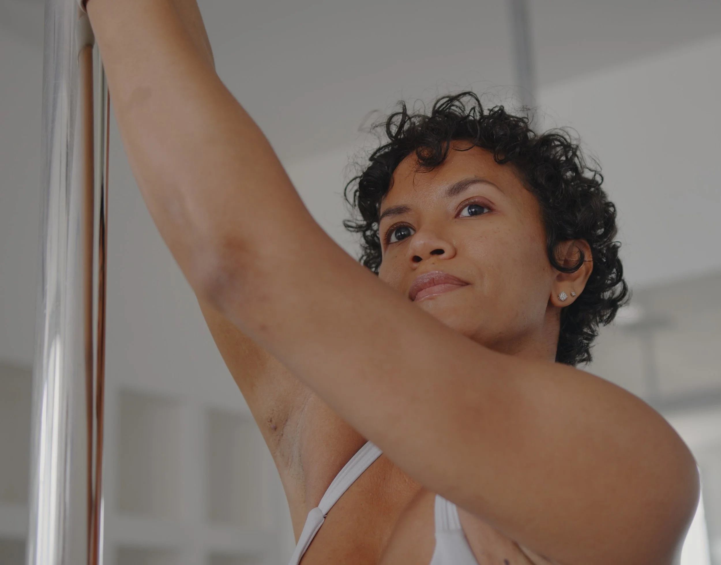 Gabbie gripping a pole outdoors, her expression calm and reflective as she looks off-frame.