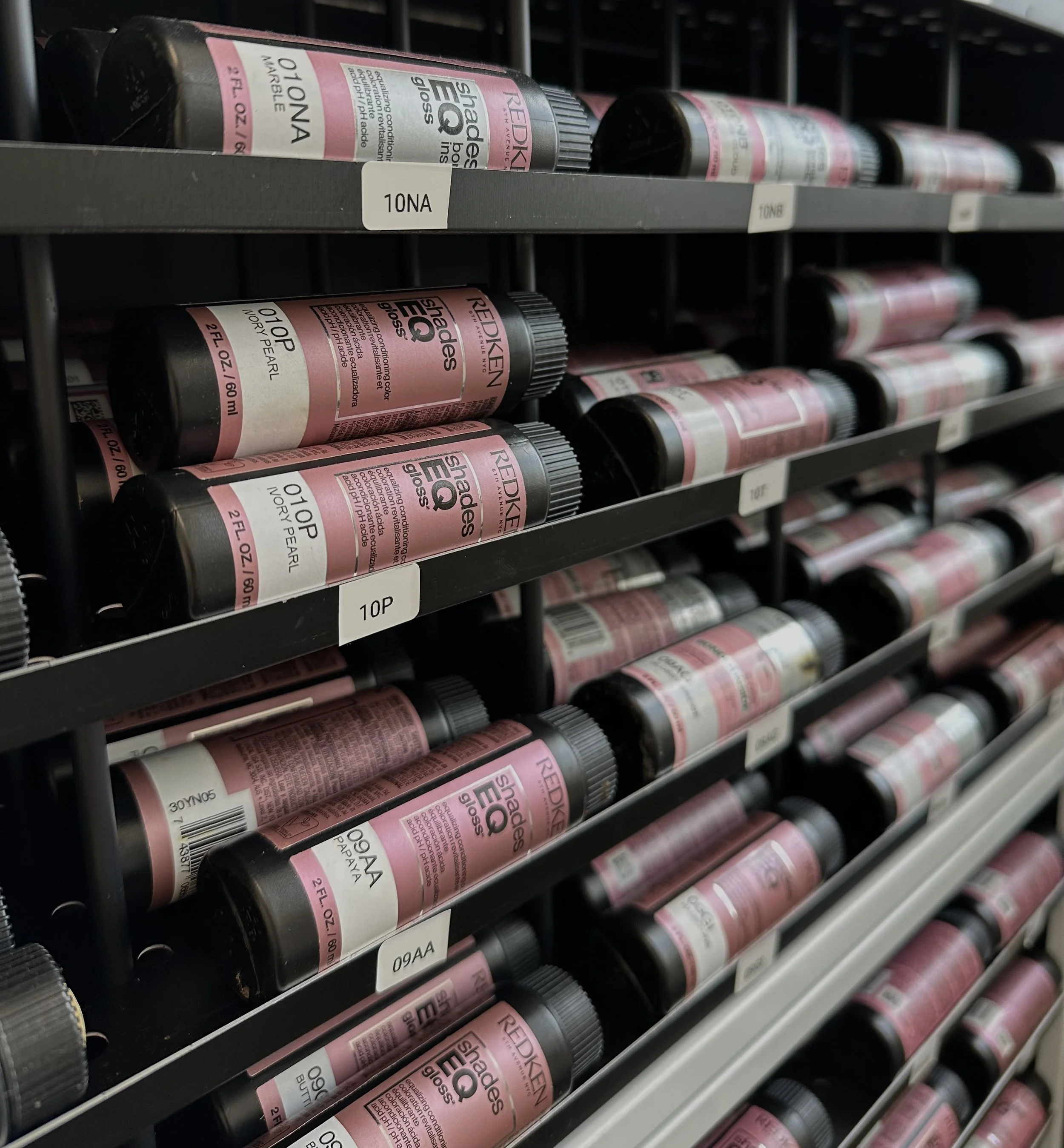 Shelf of pink and black bottles of Redken Shades EQ hair glosses in a store aisle.
