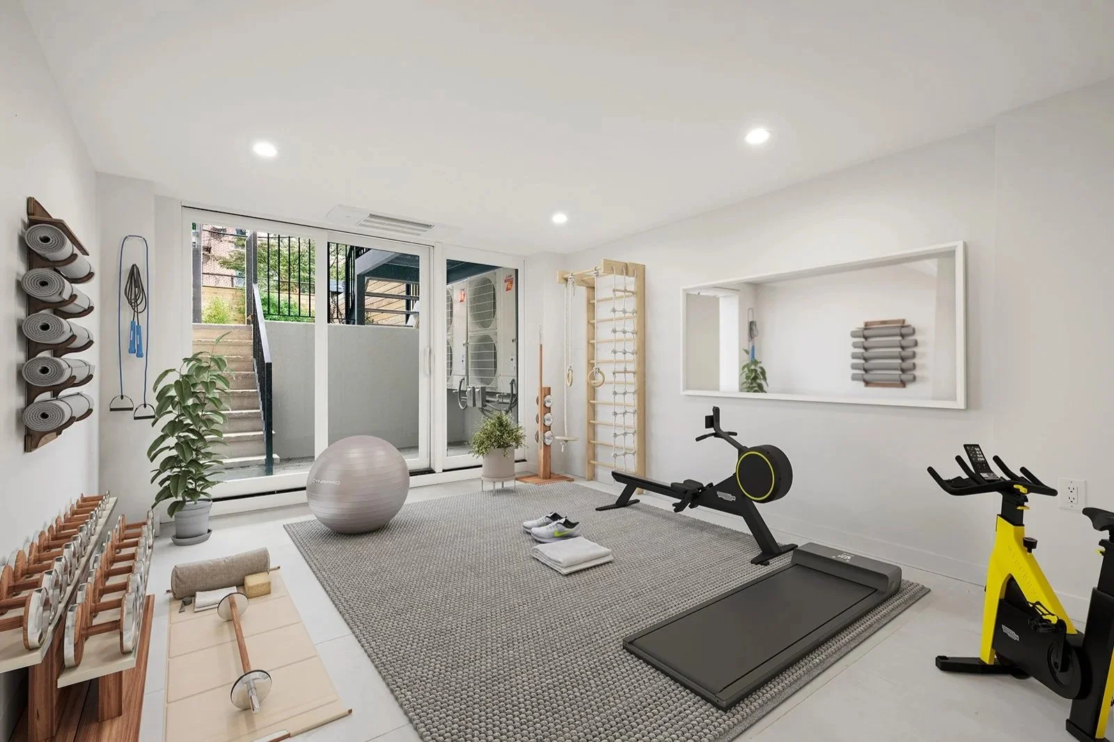 Home gym with workout equipment, yoga mats, dumbbells, exercise ball, treadmill, stationary bike, wooden climbing wall, and sliding glass door leading to outdoor stairs.