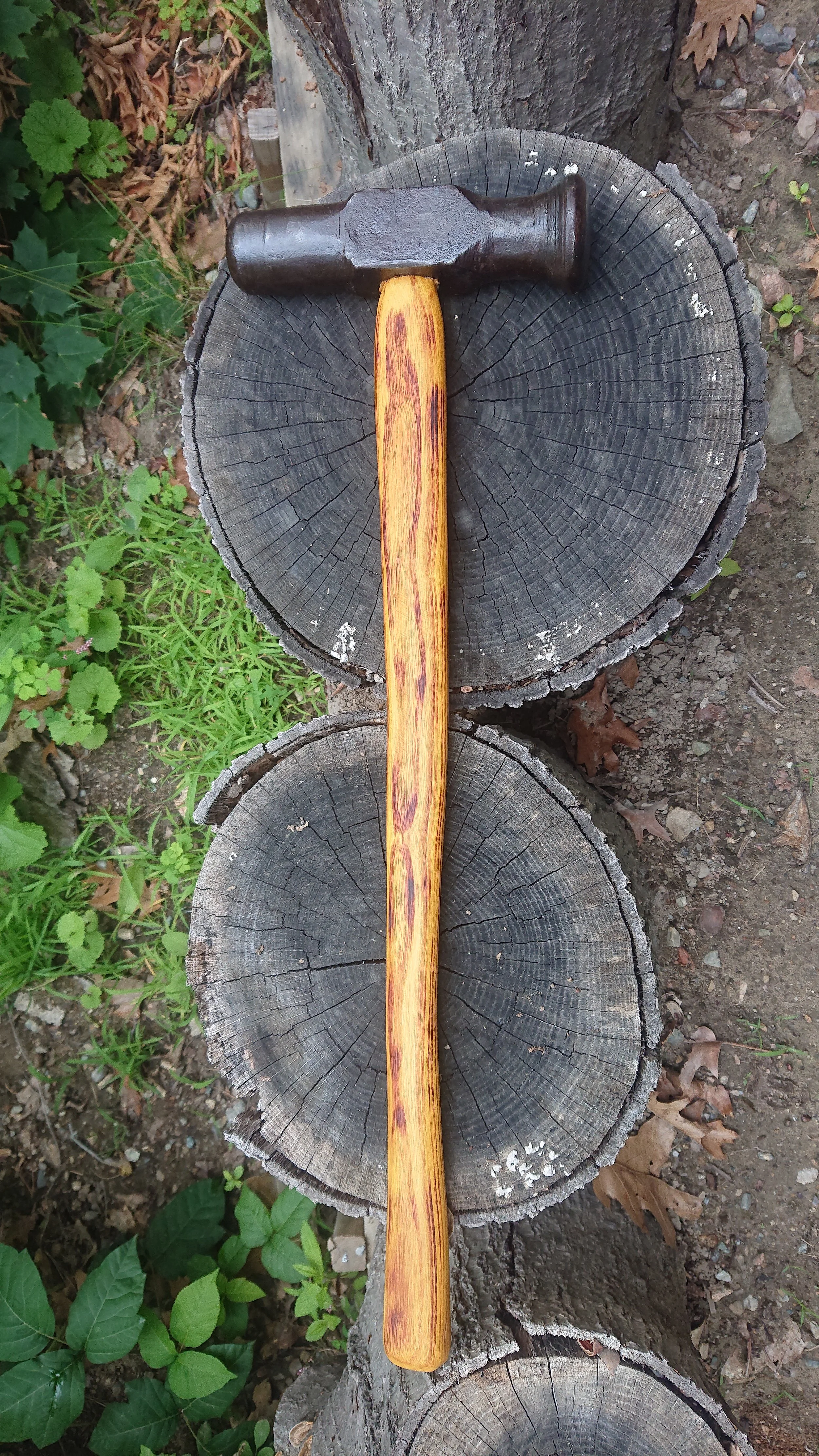 A hammer resting on stacked wooden logs outdoors with green plants around.