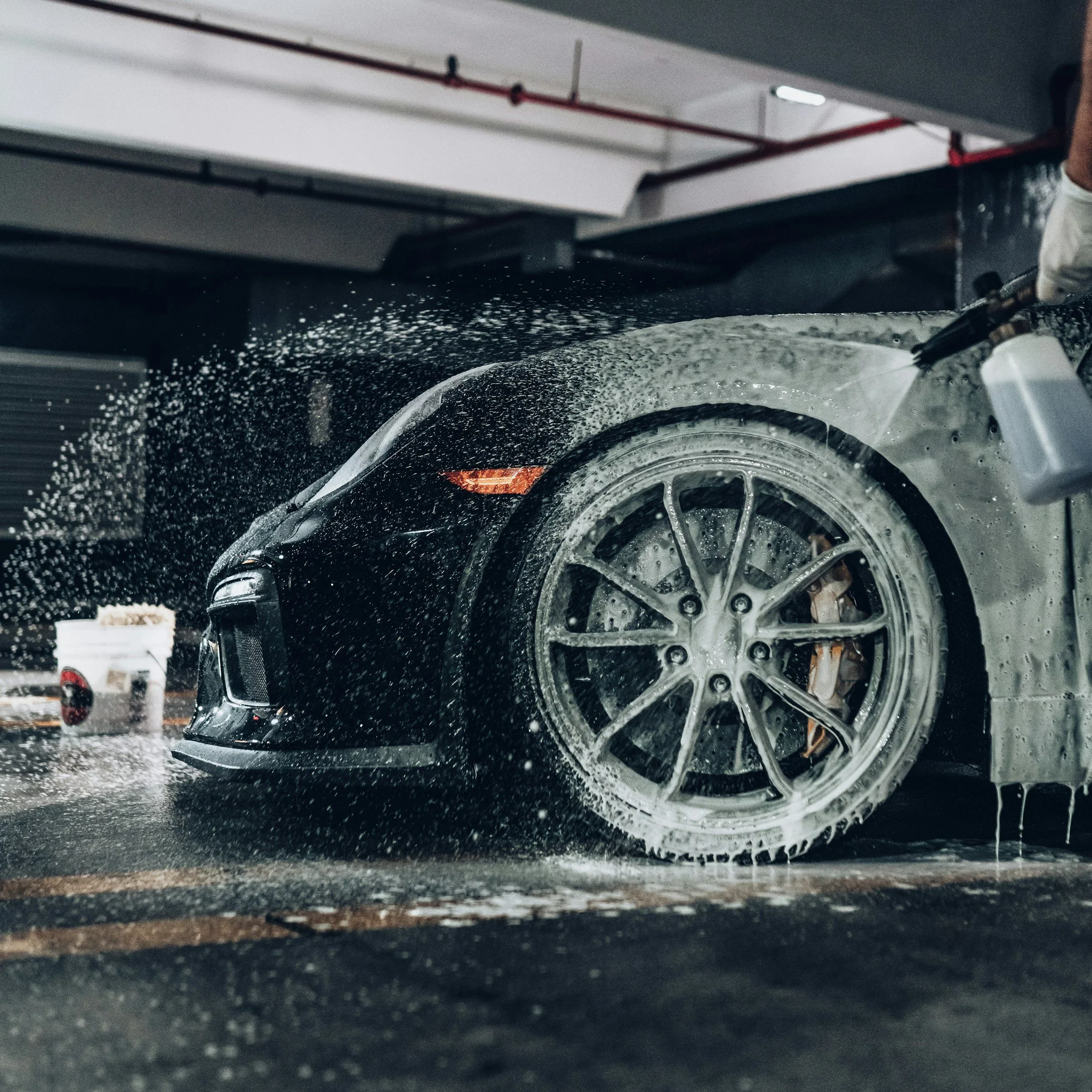 Car being washed with water spray in an indoor garage.