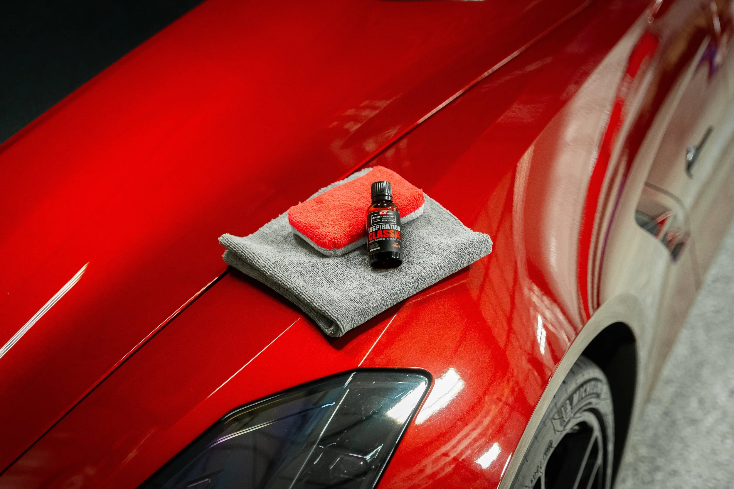 Red sports car with a towel, red applicator pad, and a bottle of car polish on the hood.