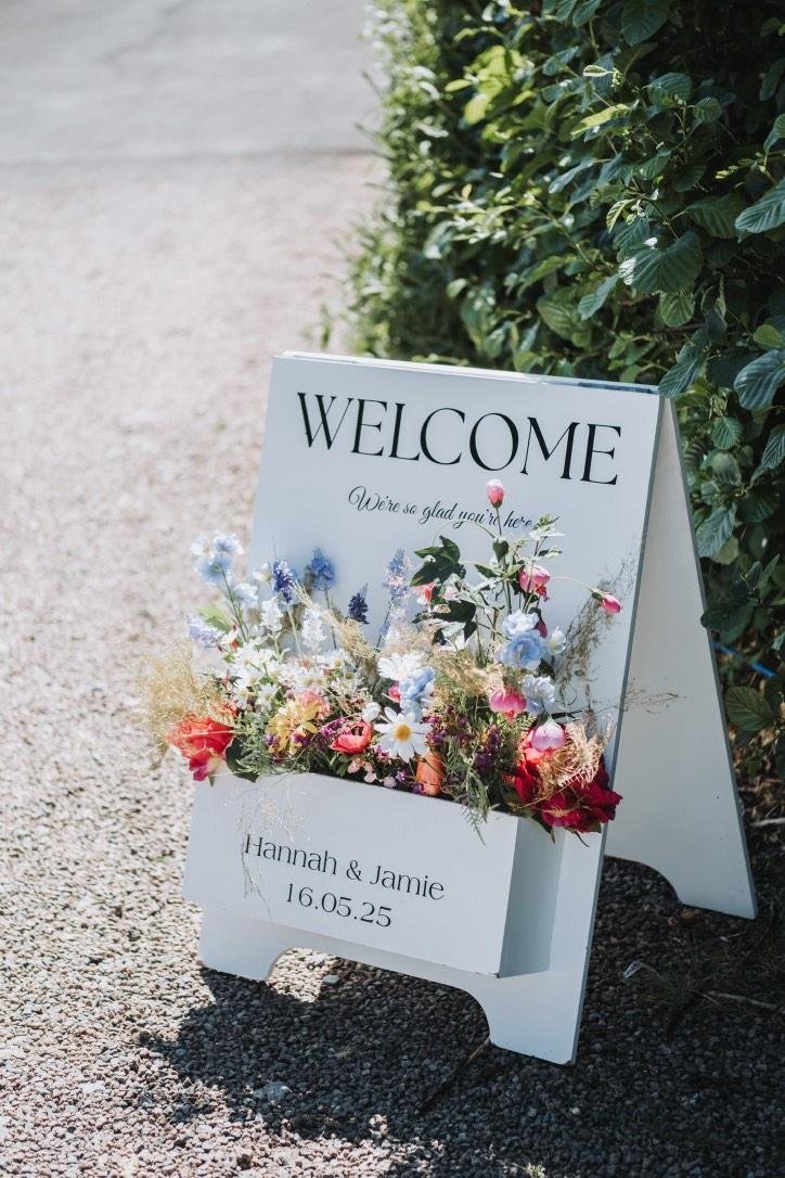 Welcoming sign with floral arrangements for Hannah and Jamie's event on May 16, 2025 at Harveys Point Donegal.