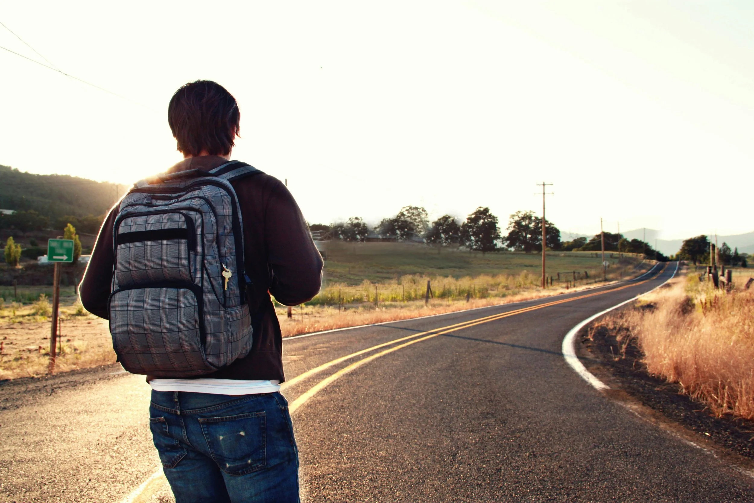 Person with a backpack walking along a deserted rural road during sunset.