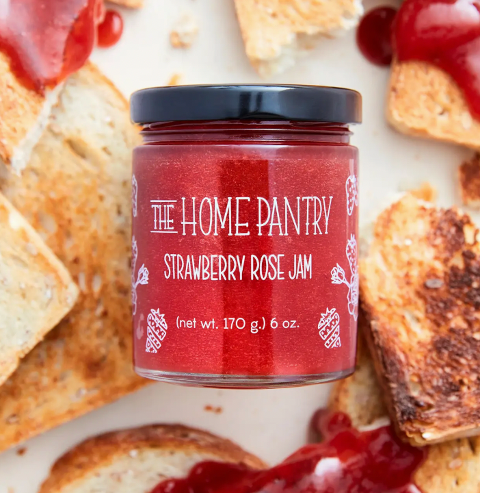 A jar of strawberry rose jam surrounded by slices of bread and dollops of strawberry jam.
