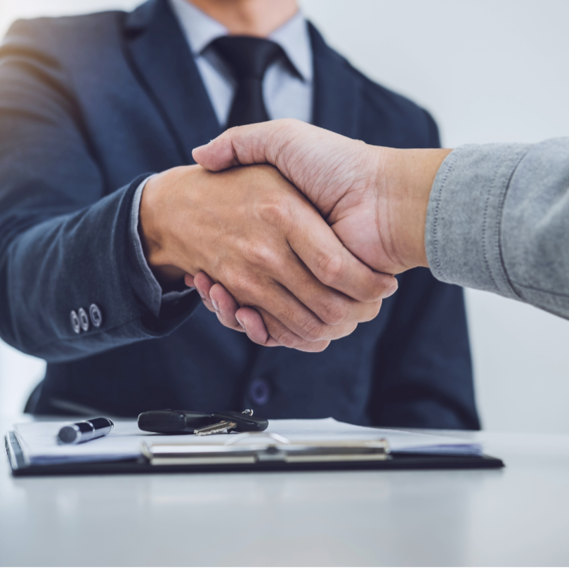 Due persone che si stringono la mano in un accordo professionale, con una scrivania con documenti e penne.
