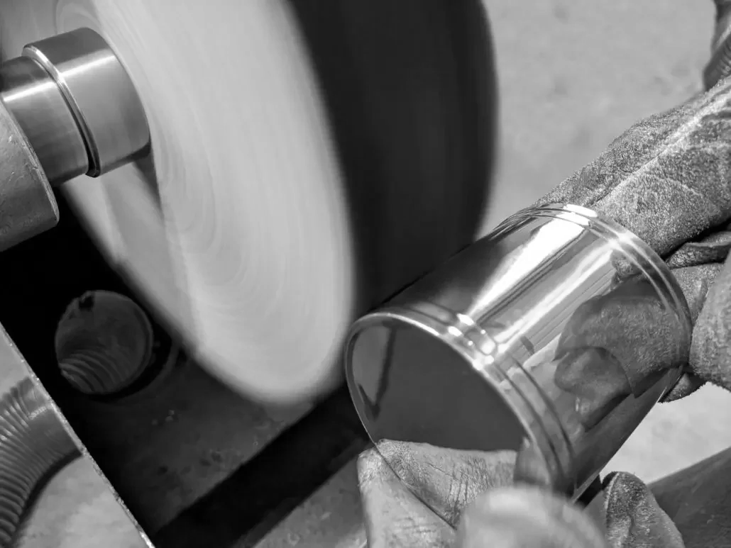 Uomo che lavora su un tornio, lucidando un bicchiere di metallo.