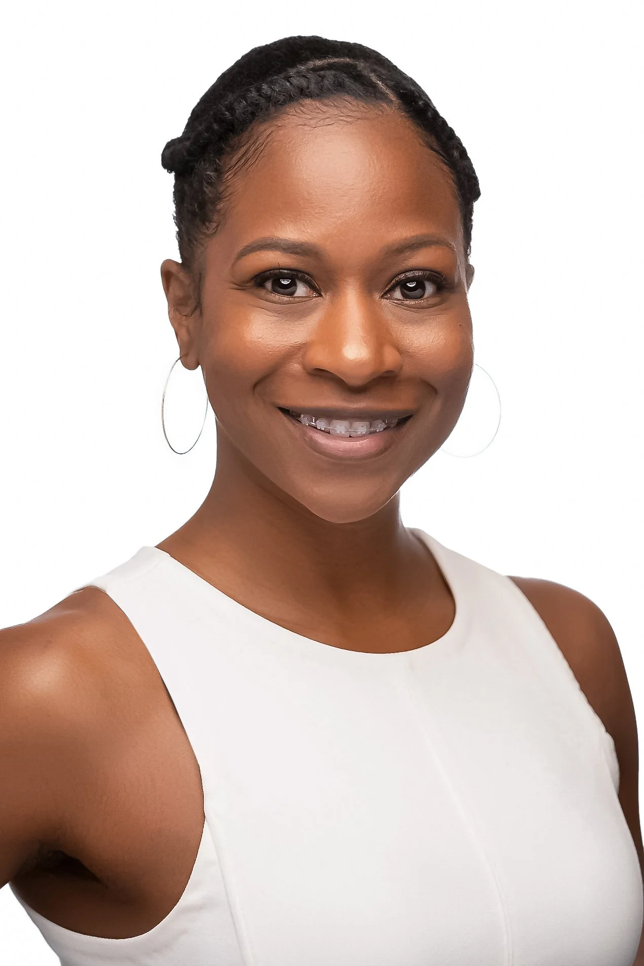 A smiling African American woman with braided hair, wearing a sleeveless white top and hoop earrings, against a plain white background.
