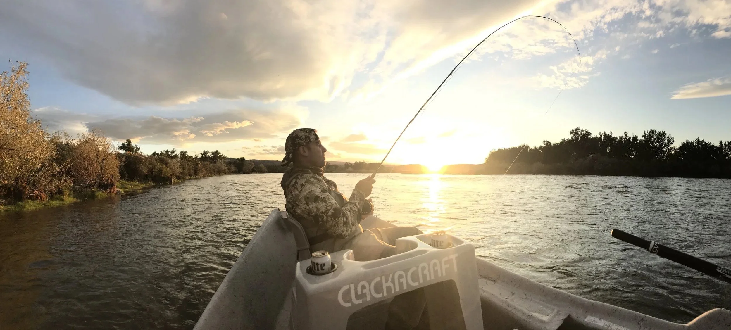 Person fishing from a small boat on a river during sunset.