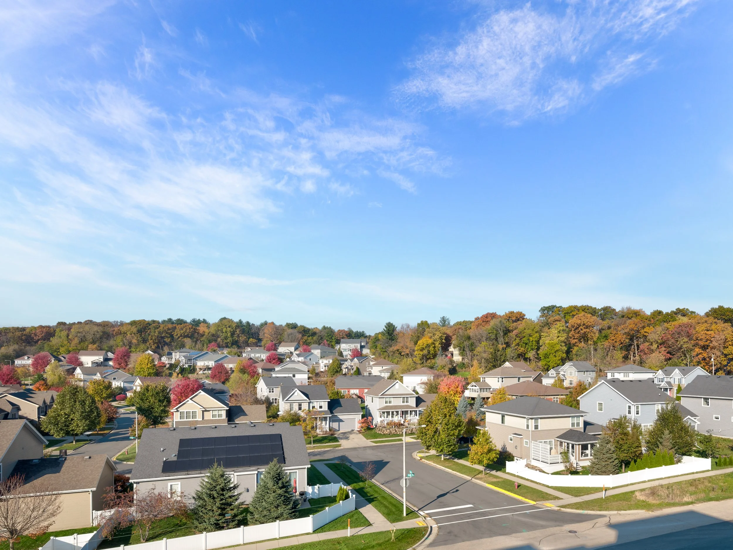 A suburban neighborhood with houses, trees, and a clear blue sky with some clouds.