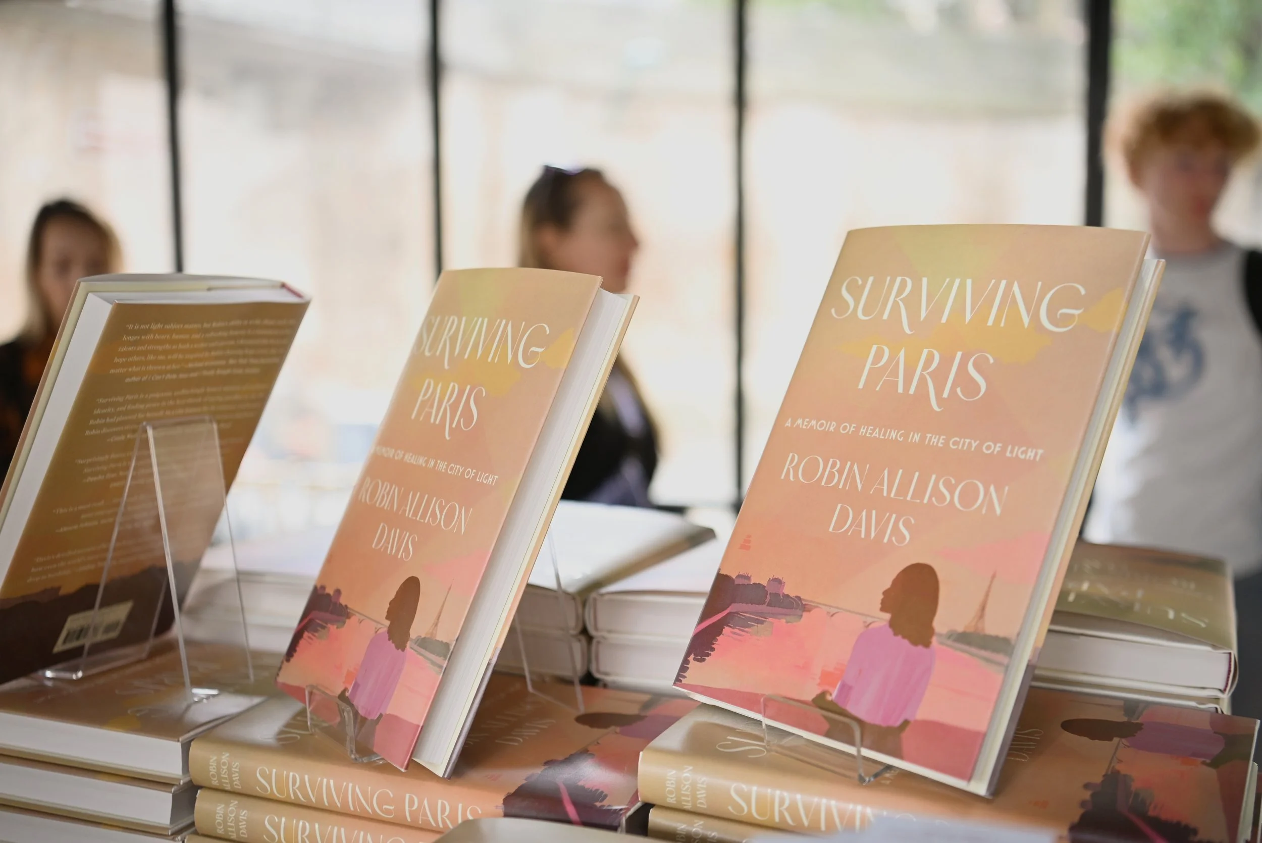 Books titled "Surviving Paris" by Robin Allison Davis on display at a bookstore, with a blurred background of people.