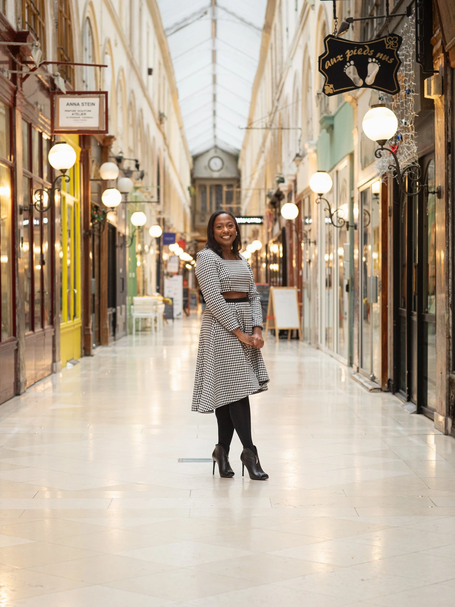 A woman standing and smiling in a covered shopping arcade with vintage decor and illuminated signs.