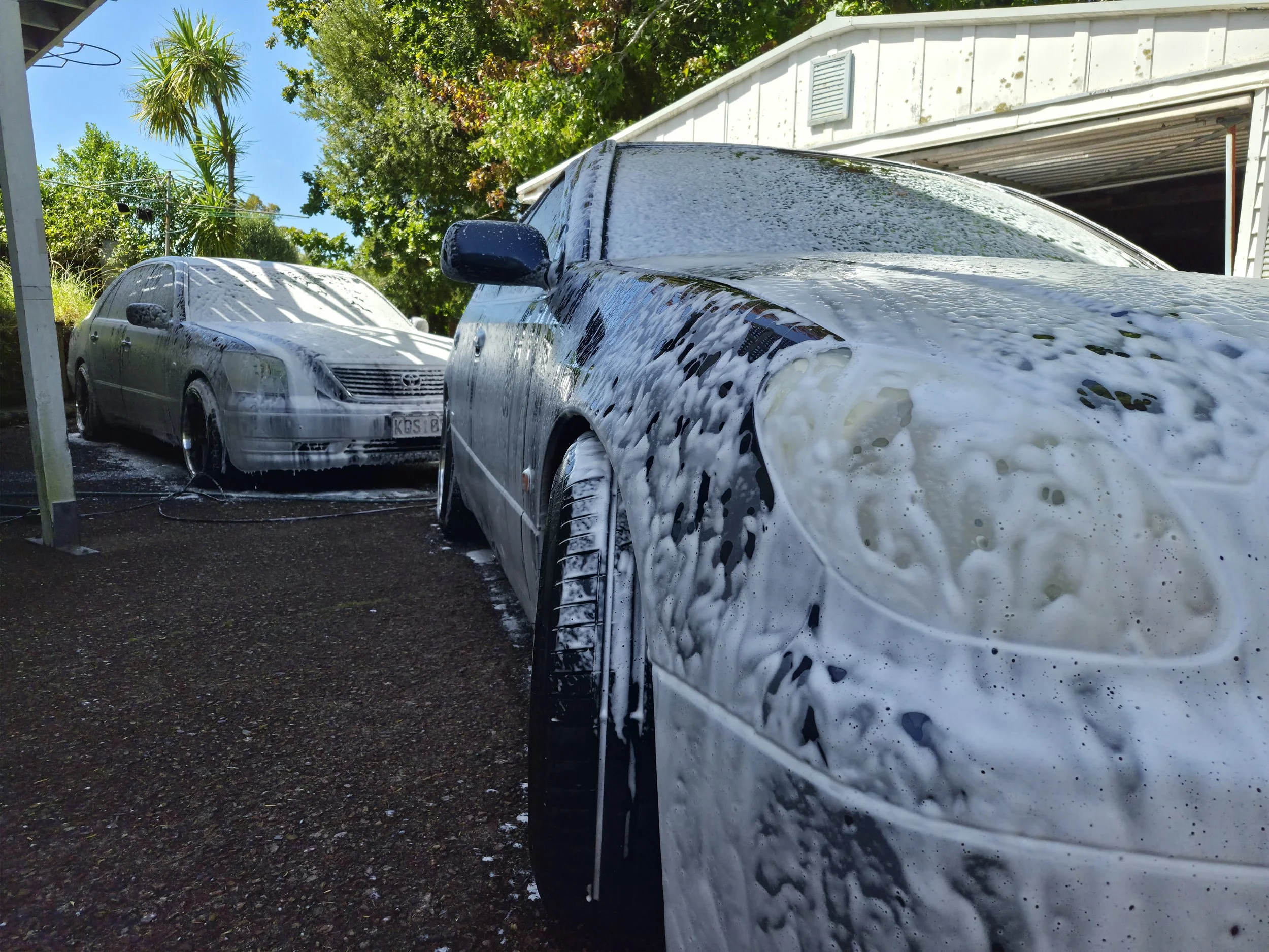 Two cars parked in a driveway being washed with soap and water, surrounded by trees and a white garage.