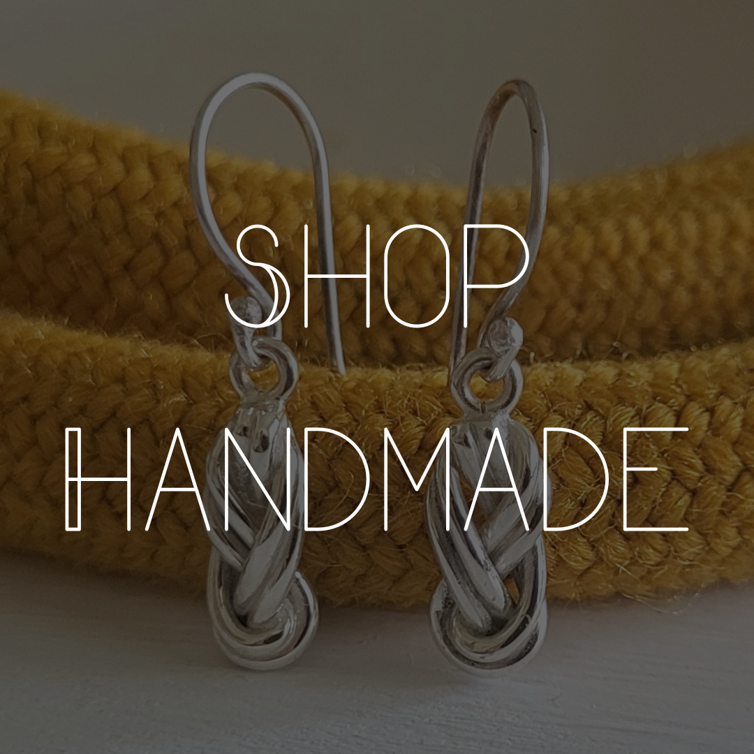A pair of silver dangle earrings shaped like climbing knots rest against a yellow climbing rope.
