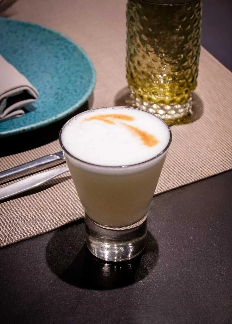 Copa con bebida cremosa y espumosa, decorada con un toque de canela o polvo marrón claro.