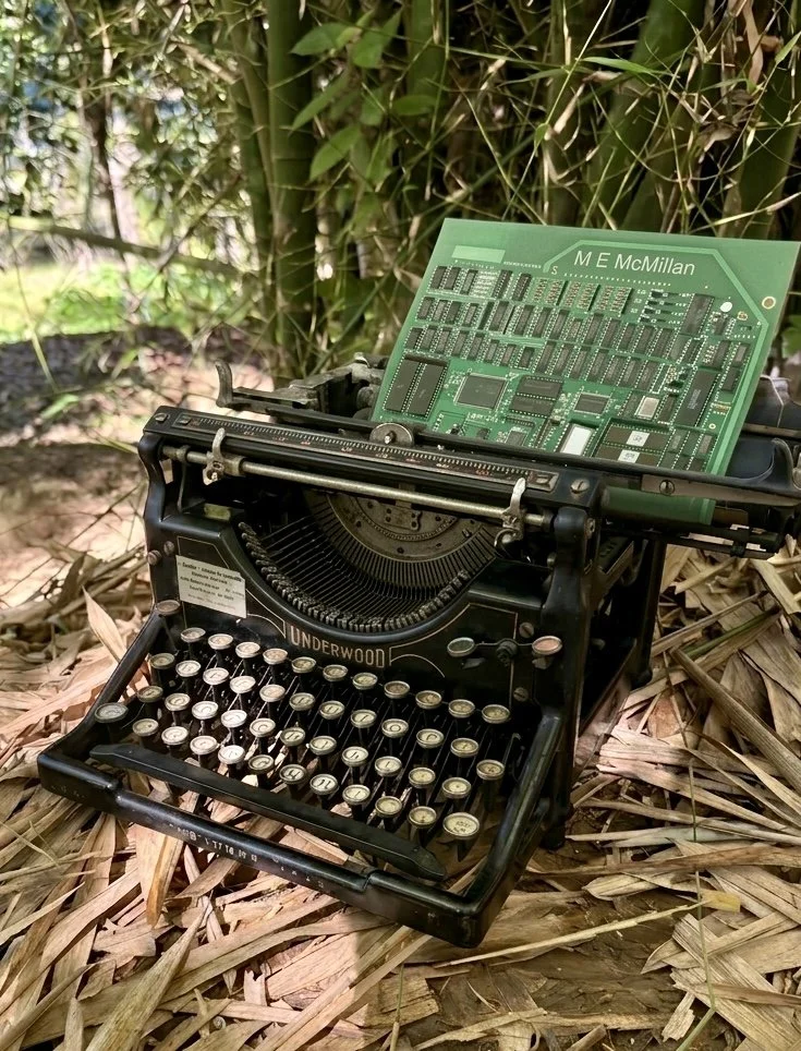 A vintage Underwood typewriter with a circuit board on top, set outdoors on dry leaves with bamboo plants in the background.