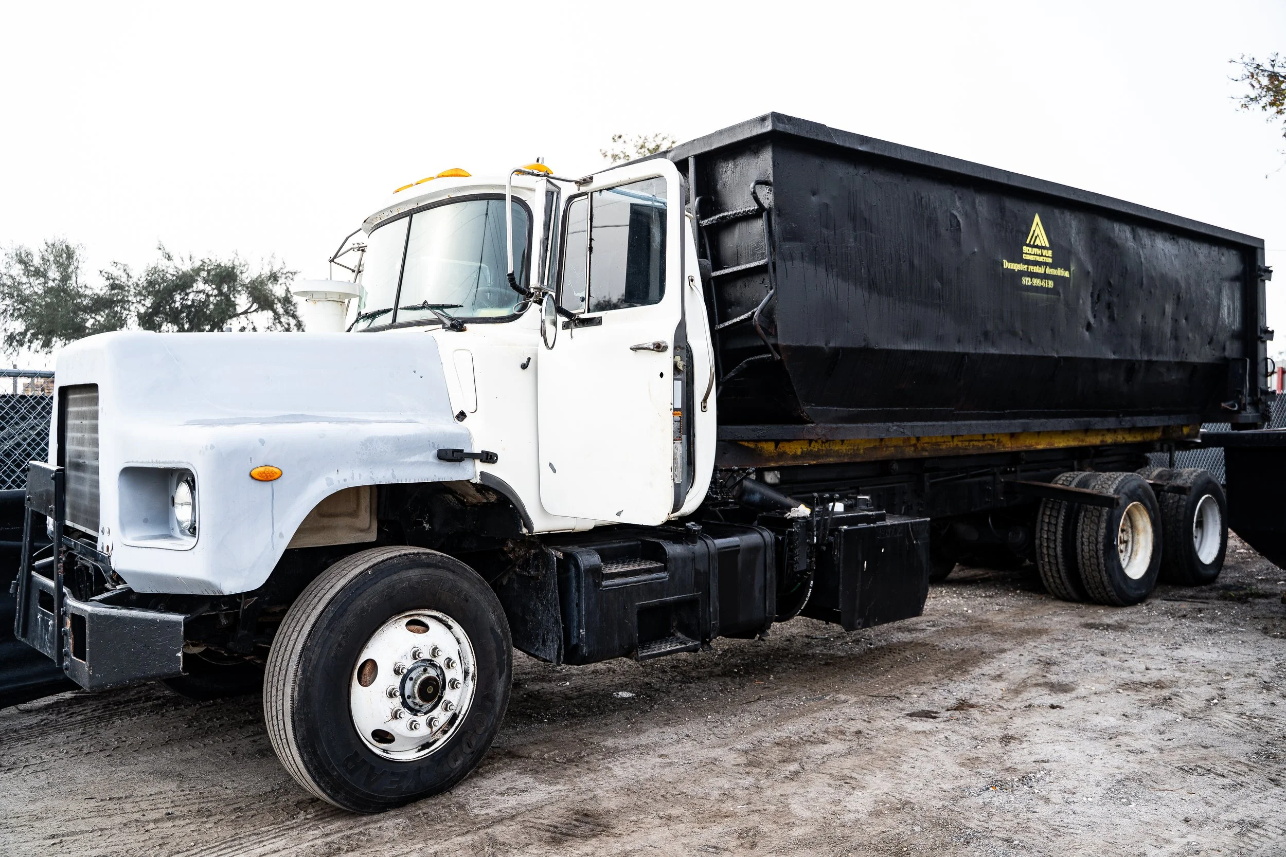 White truck with black container bed parked on a dirt lot.