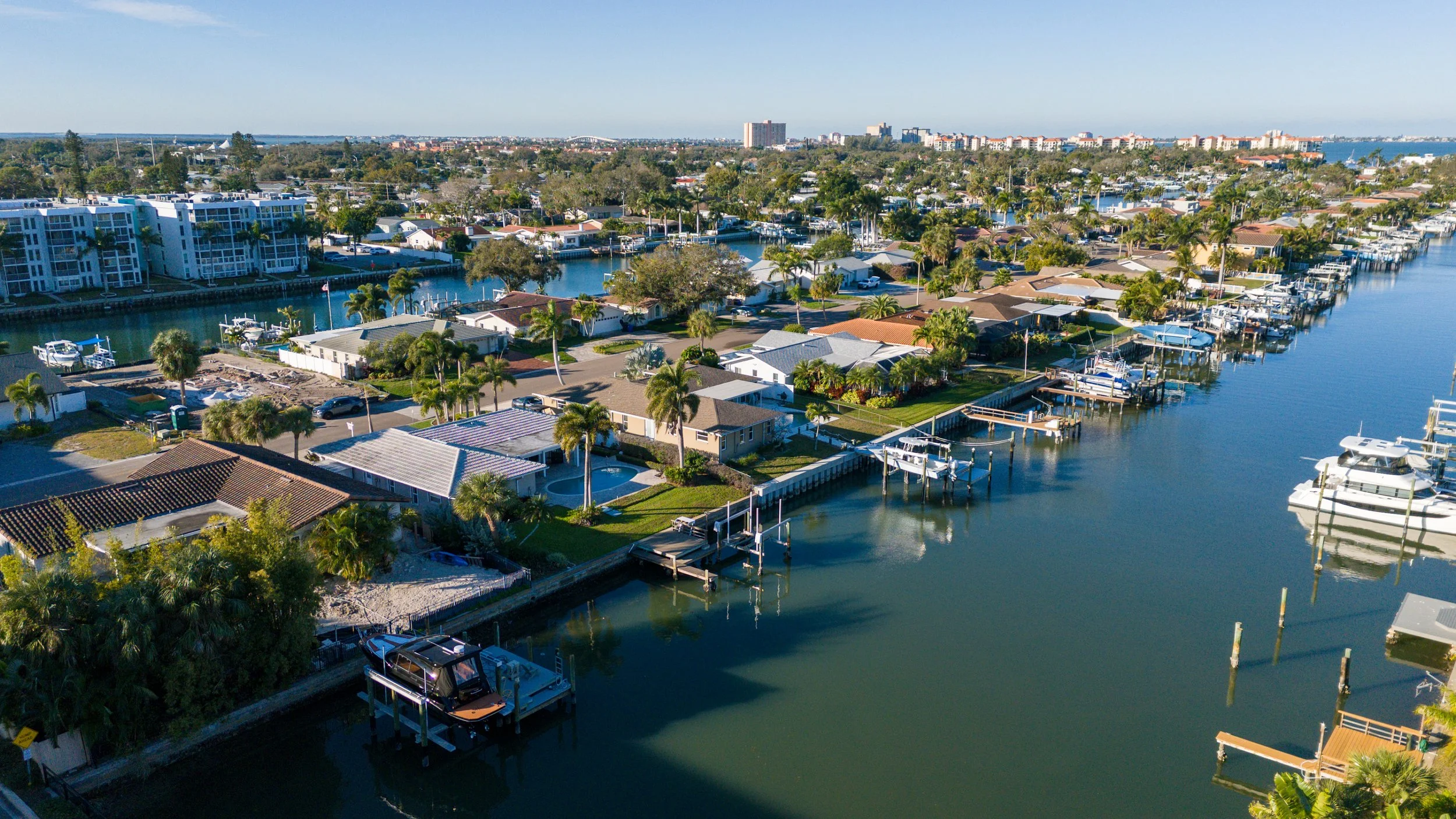Aerial view of a residential neighborhood along a canal with boats and docks, with multi-story buildings and trees in the background.