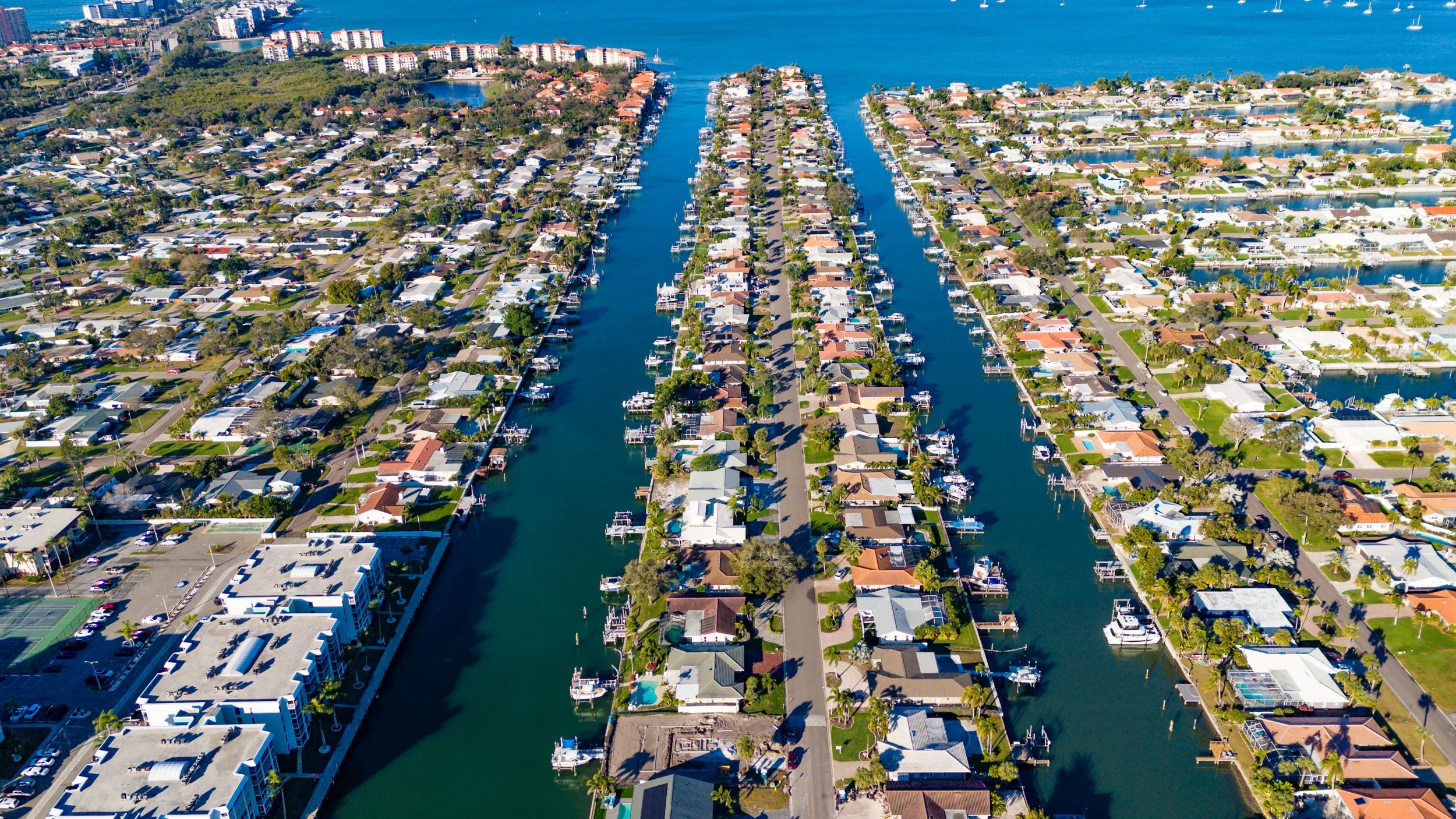 Aerial view of residential houses lining a canal with boats docked on both sides in a coastal city.