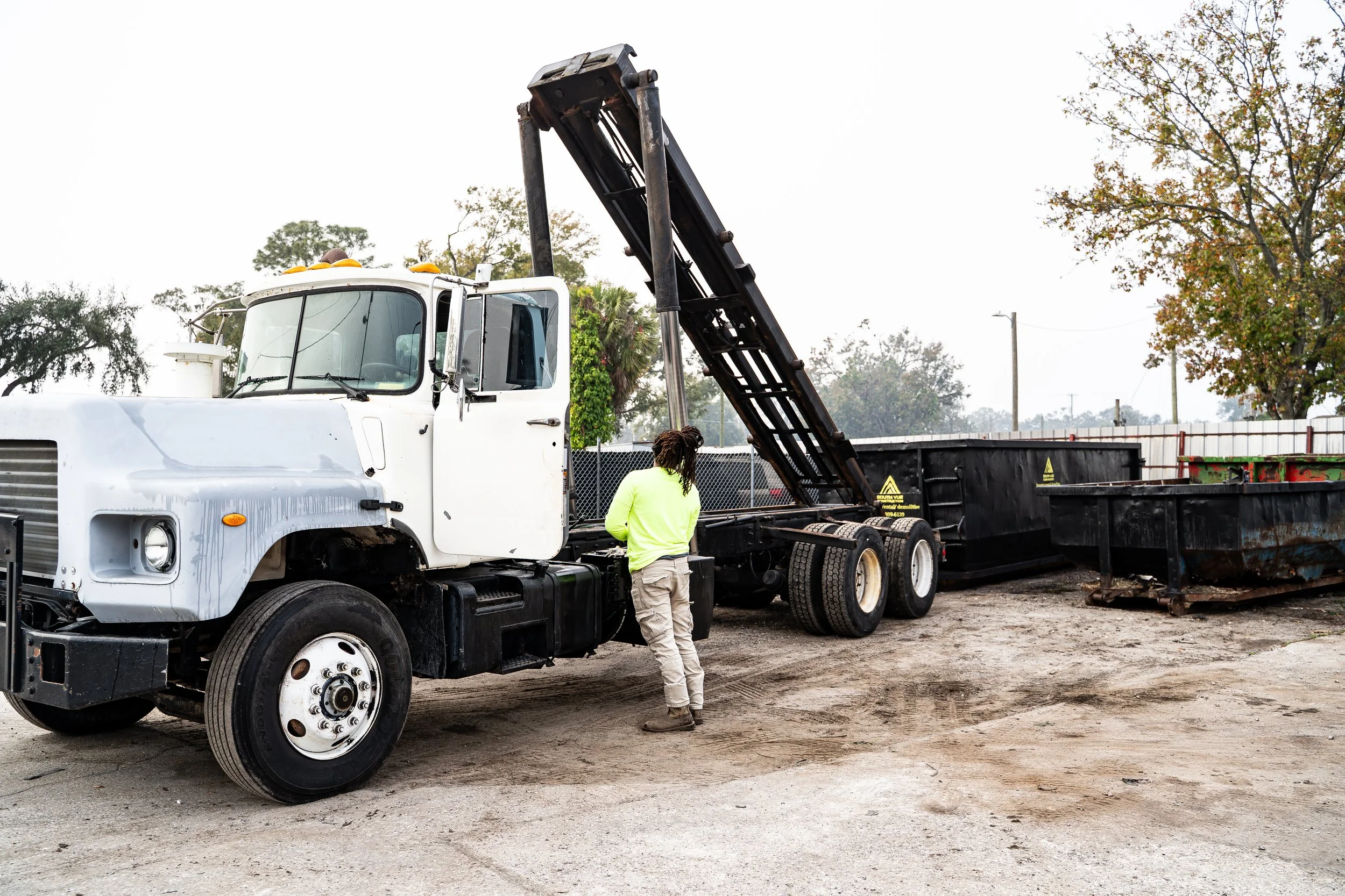 Person standing next to a white and black dump truck with the bed raised.