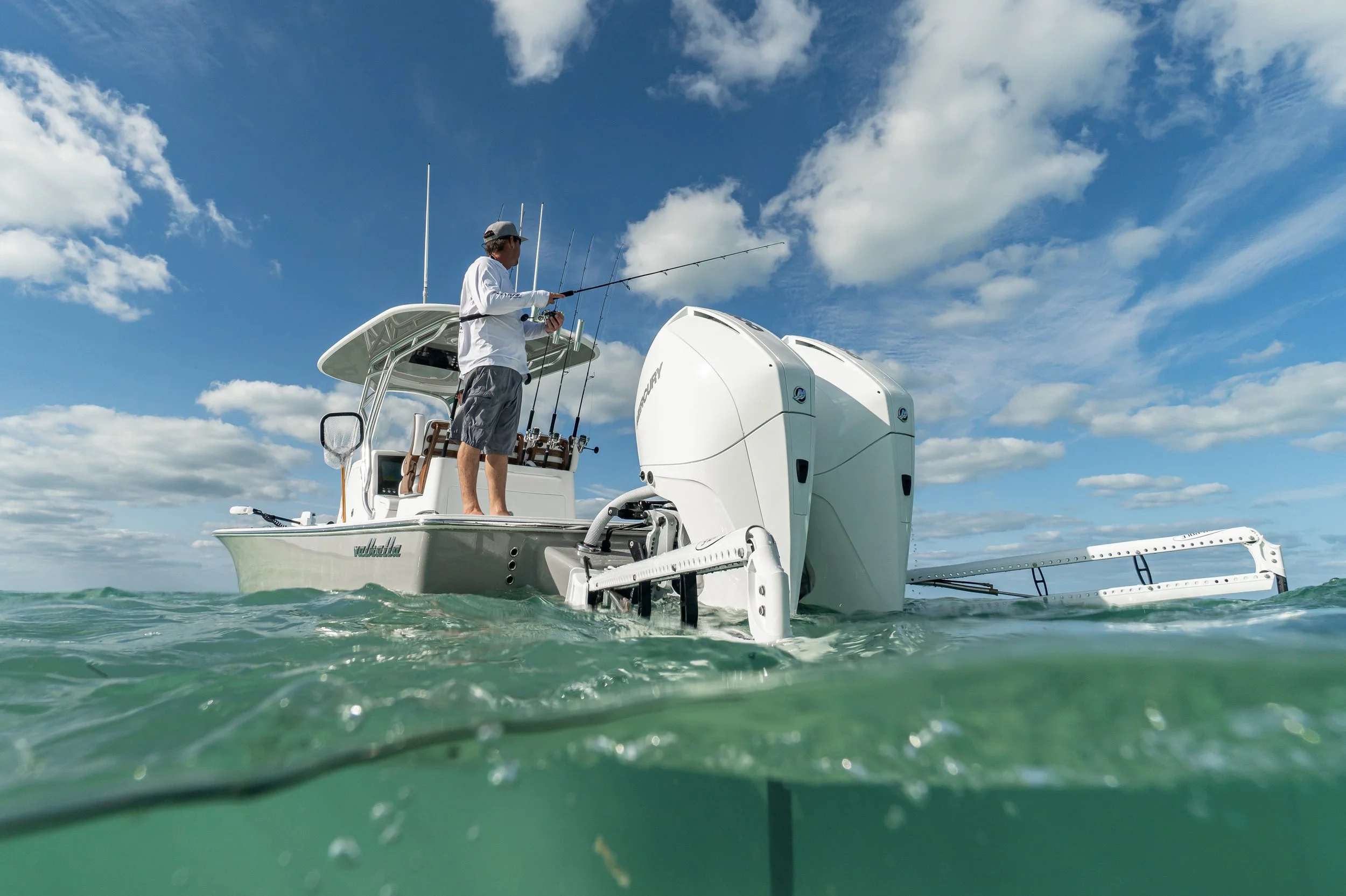 Man fishing on a boat with a large outboard motor in the ocean, under a partly cloudy sky.