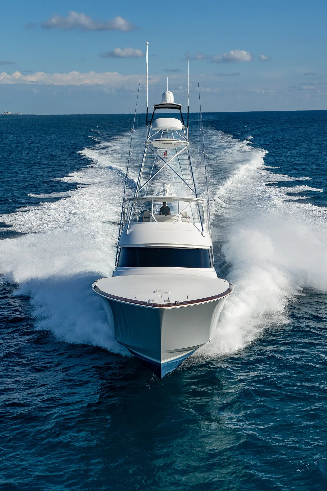 A white yacht sailing through the ocean, creating a large wake behind it on a clear day with blue sky and some clouds.