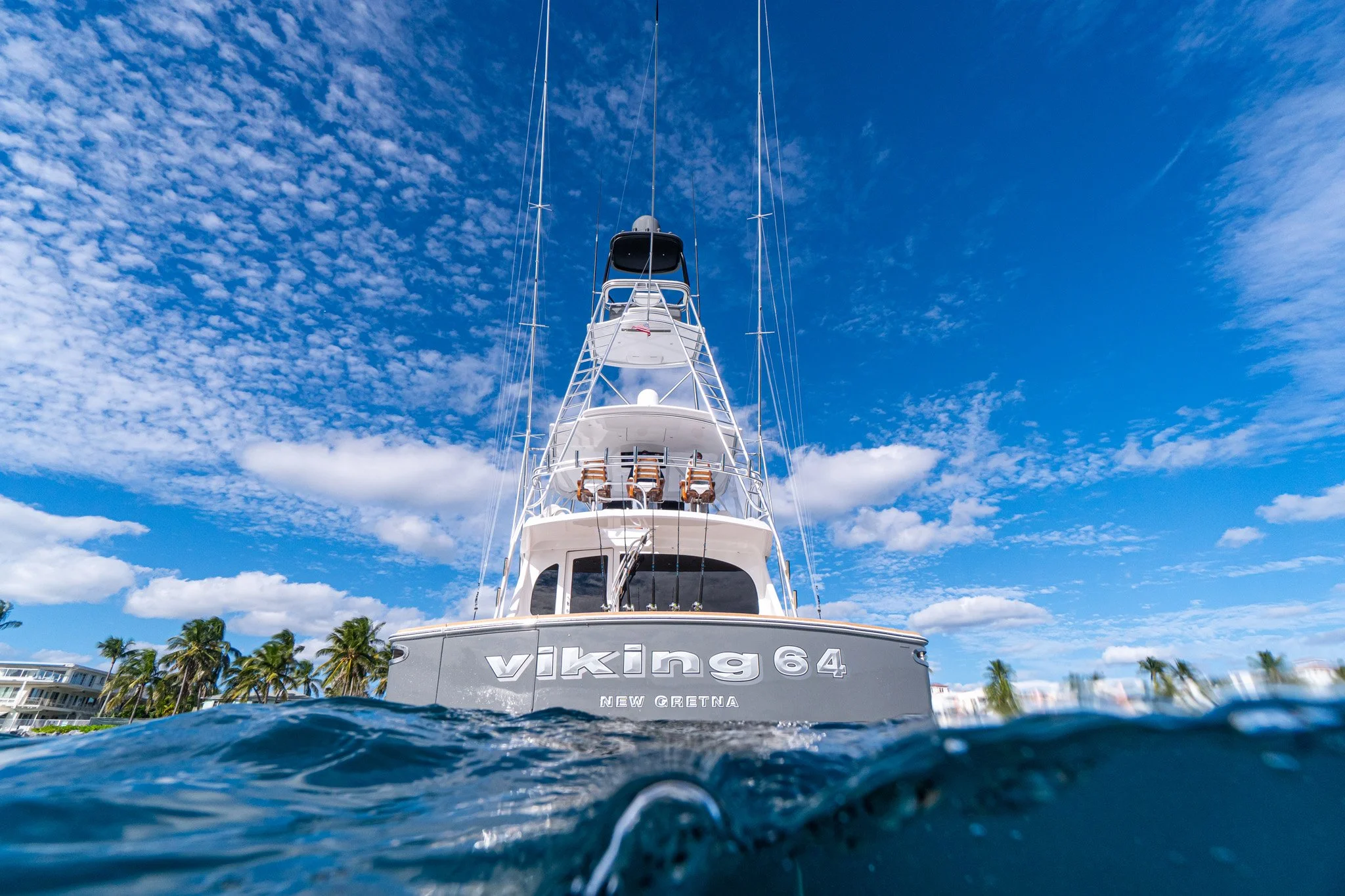 Boat named Viking 64 anchored with clear blue sky and scattered clouds, tropical palm trees along the shoreline in the background.