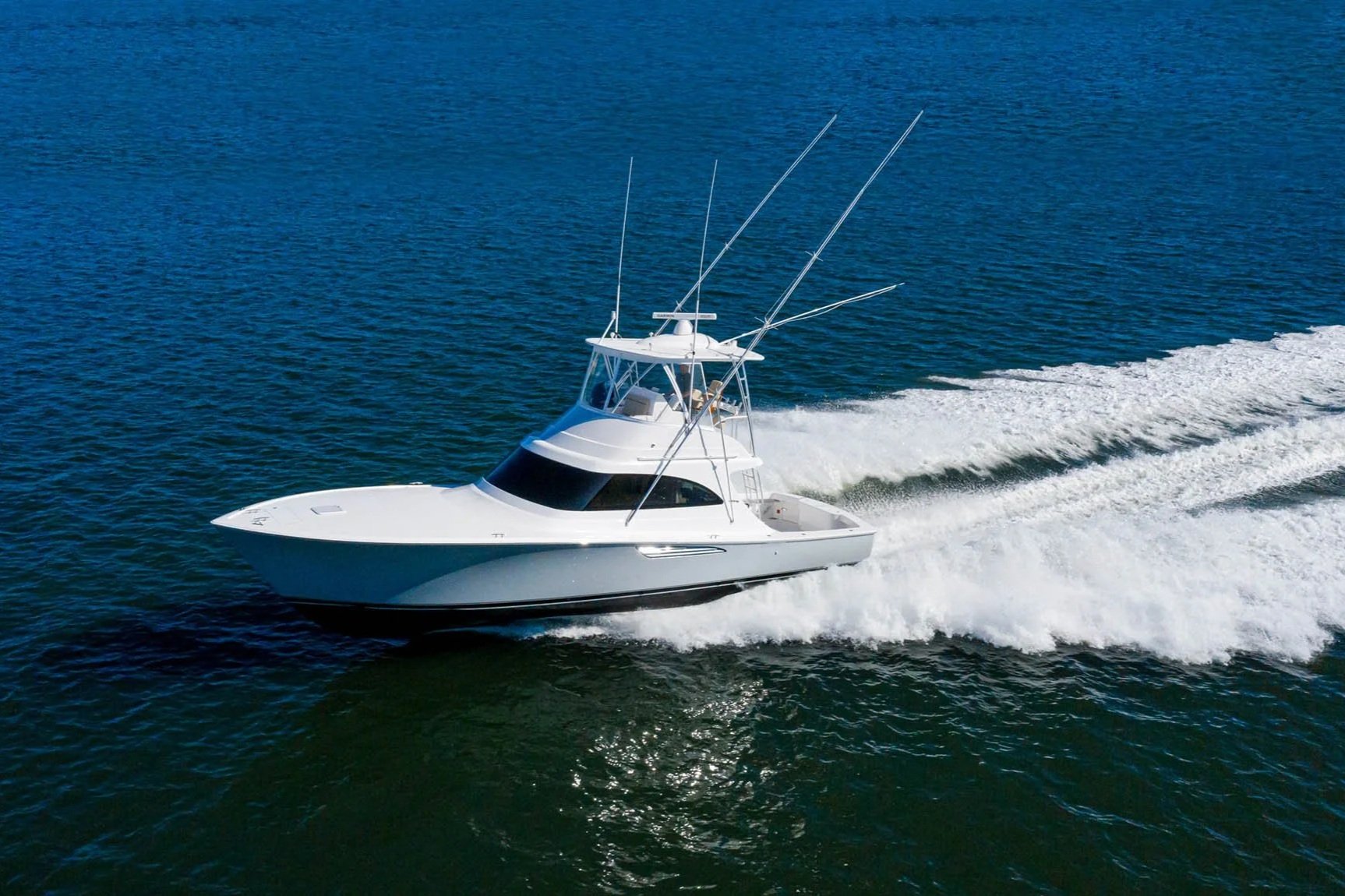 A white motor yacht speeding on the water, creating a wake behind it.