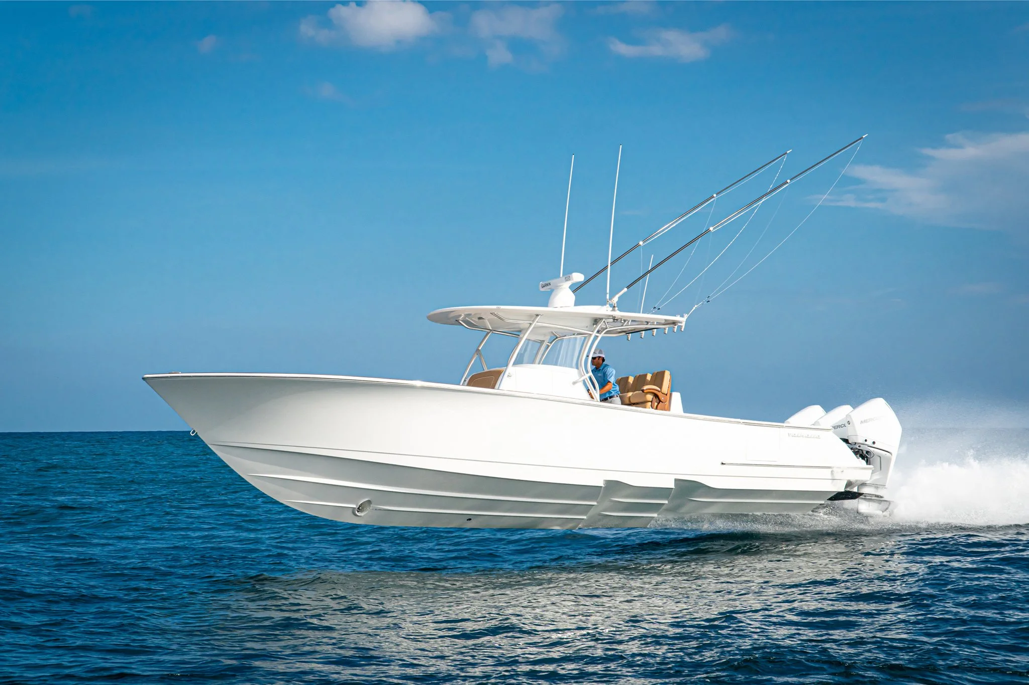 White motorboat with brown seating speeding through blue ocean under blue sky.