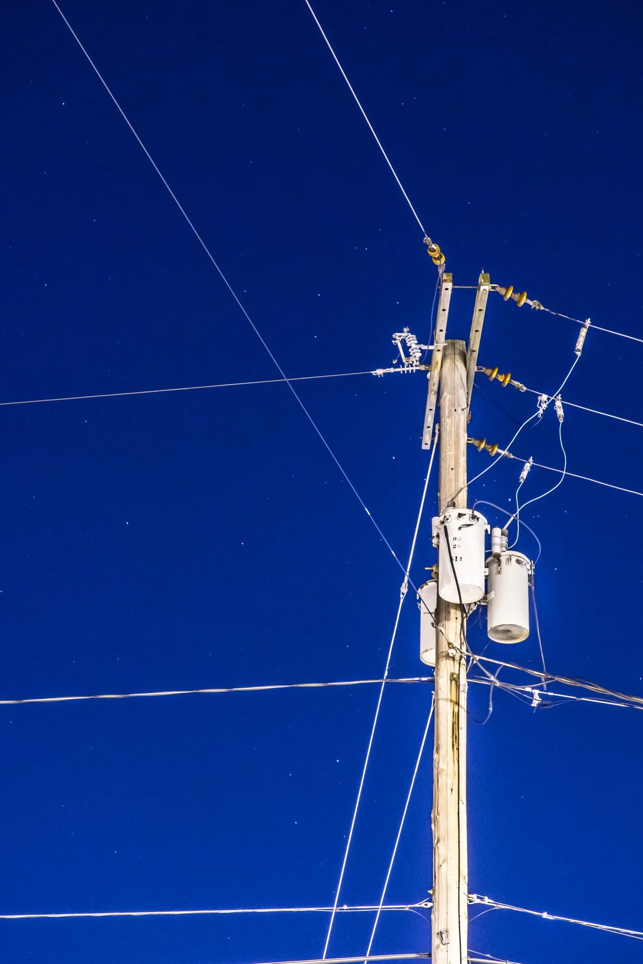 A utility pole with electrical wires and insulators against a starry night sky.