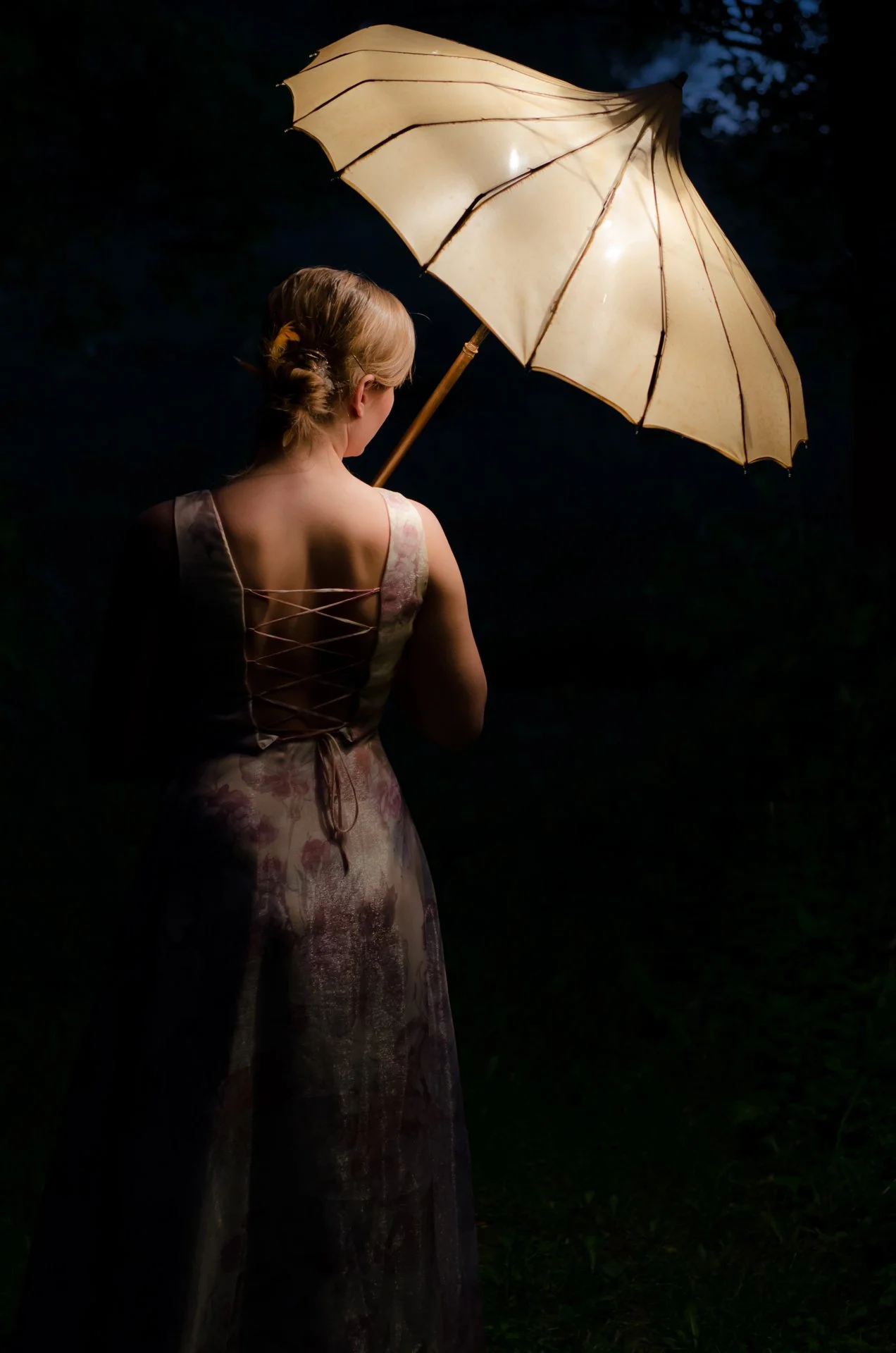 A woman standing outdoors at night holding a lit umbrella with a dark background.