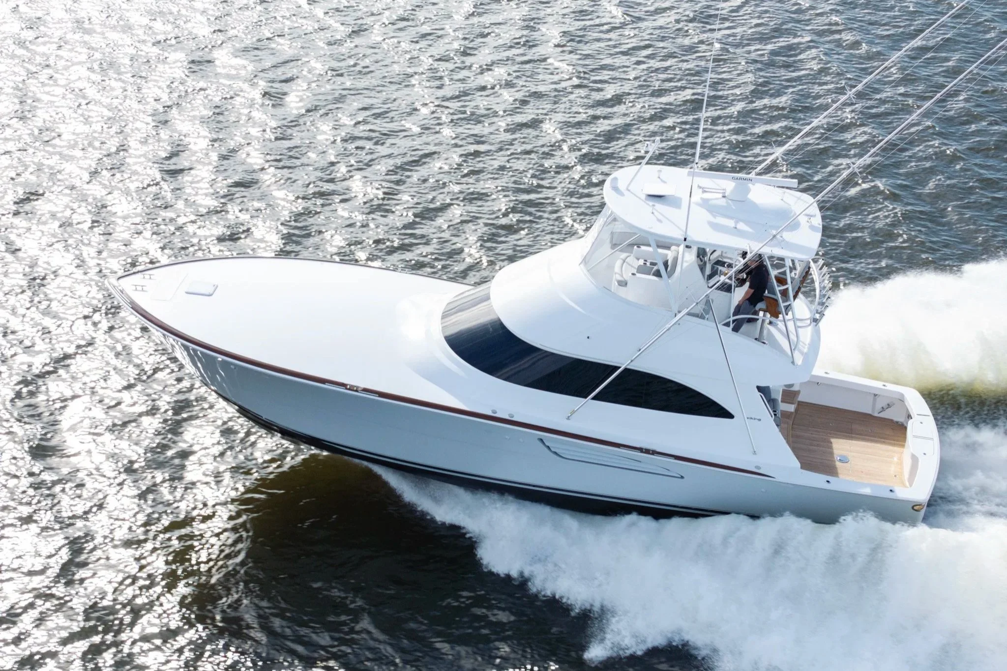 A white yacht moving through the water, creating a wake behind it, with a person visible on the deck.