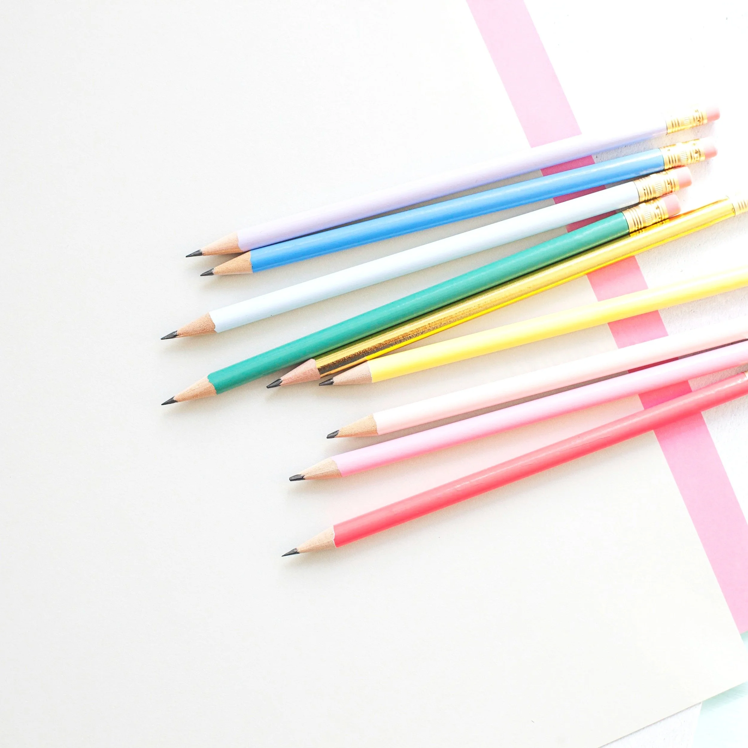 Colorful pencils arranged on white paper with pink markings.
