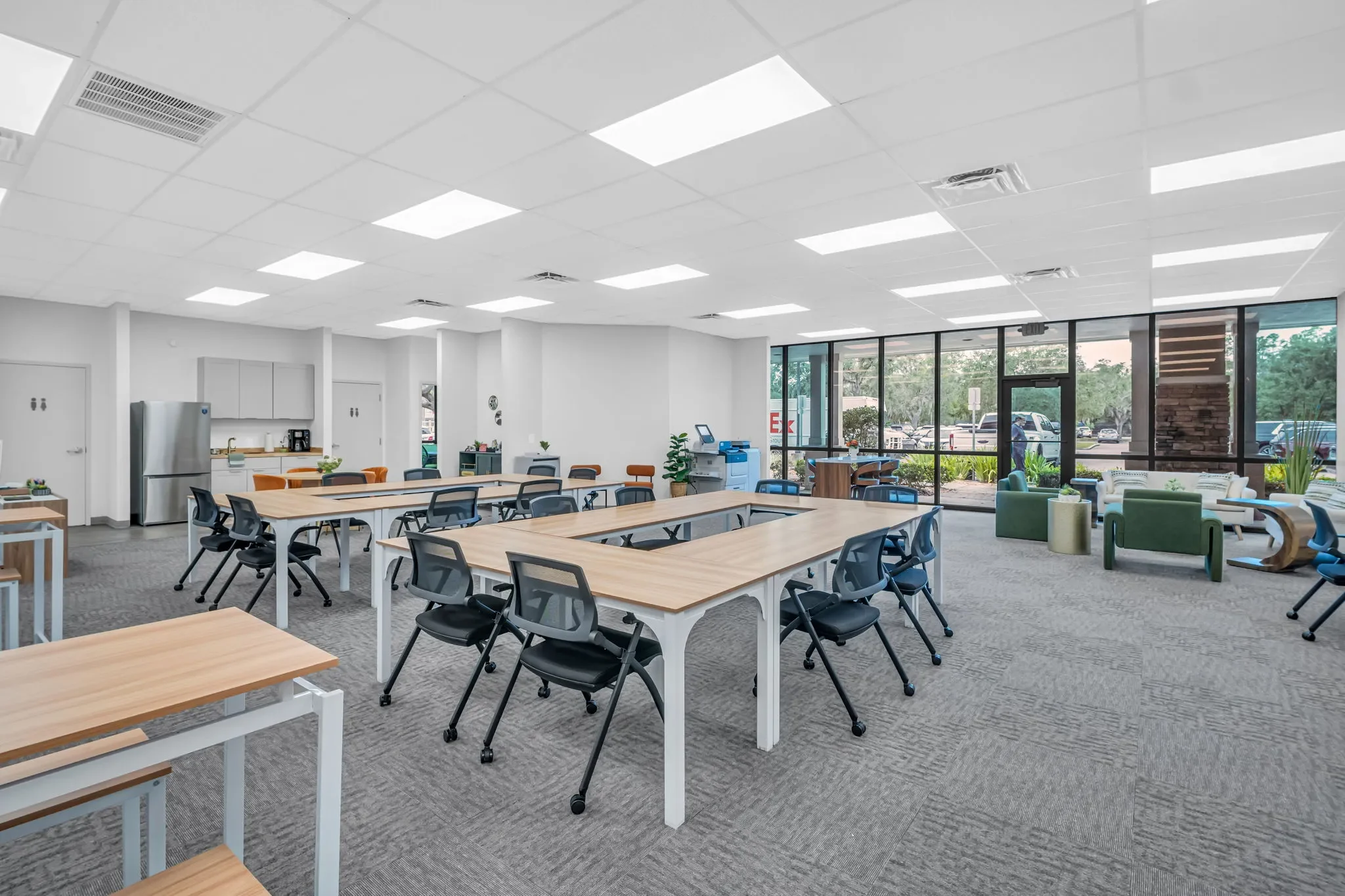 Bright, spacious room with large windows, seating area with couches, and multiple rectangular tables with chairs, set up for a meeting or community gathering.