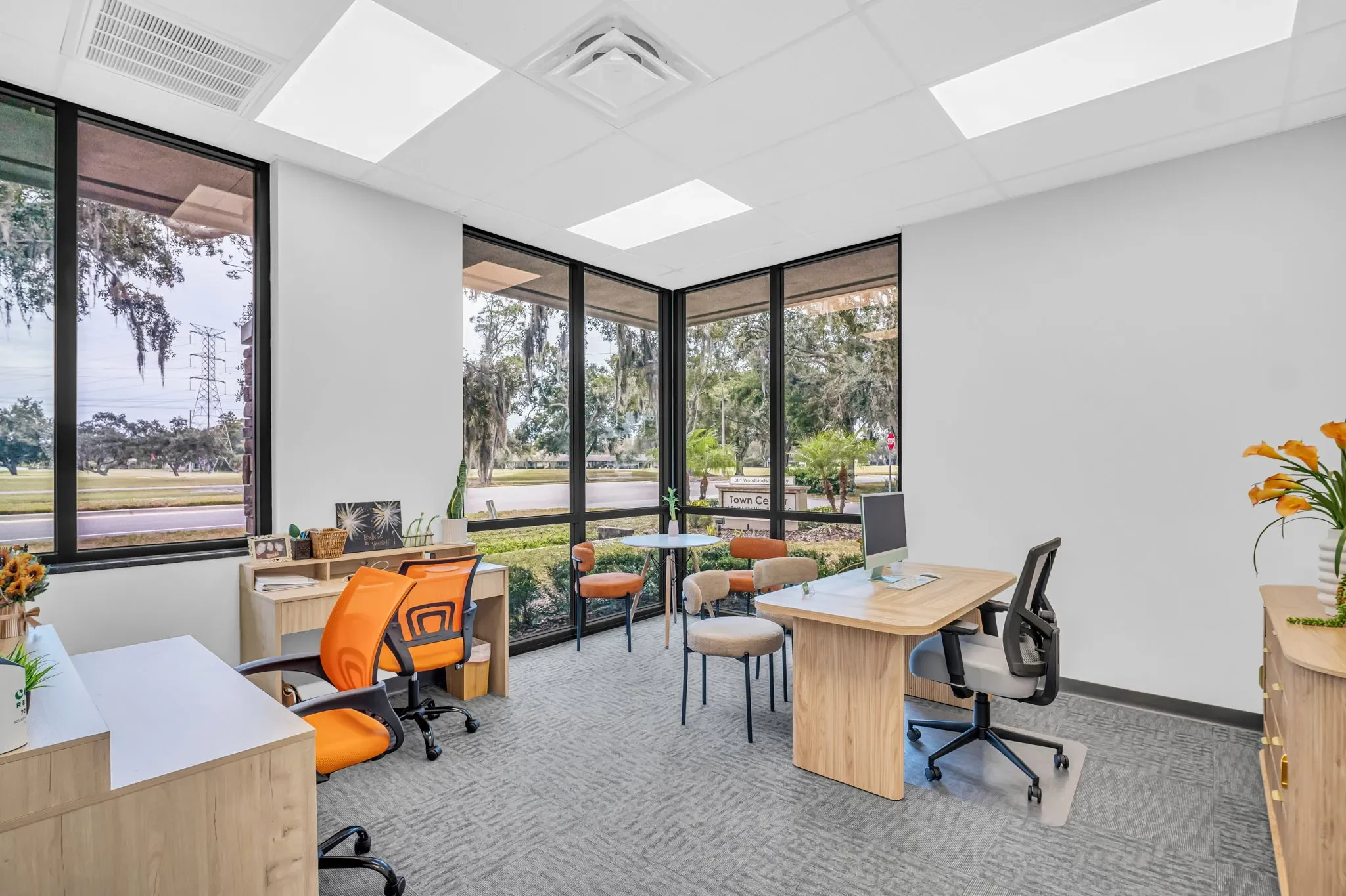 An office with large windows, two desks, several chairs, and potted plants.