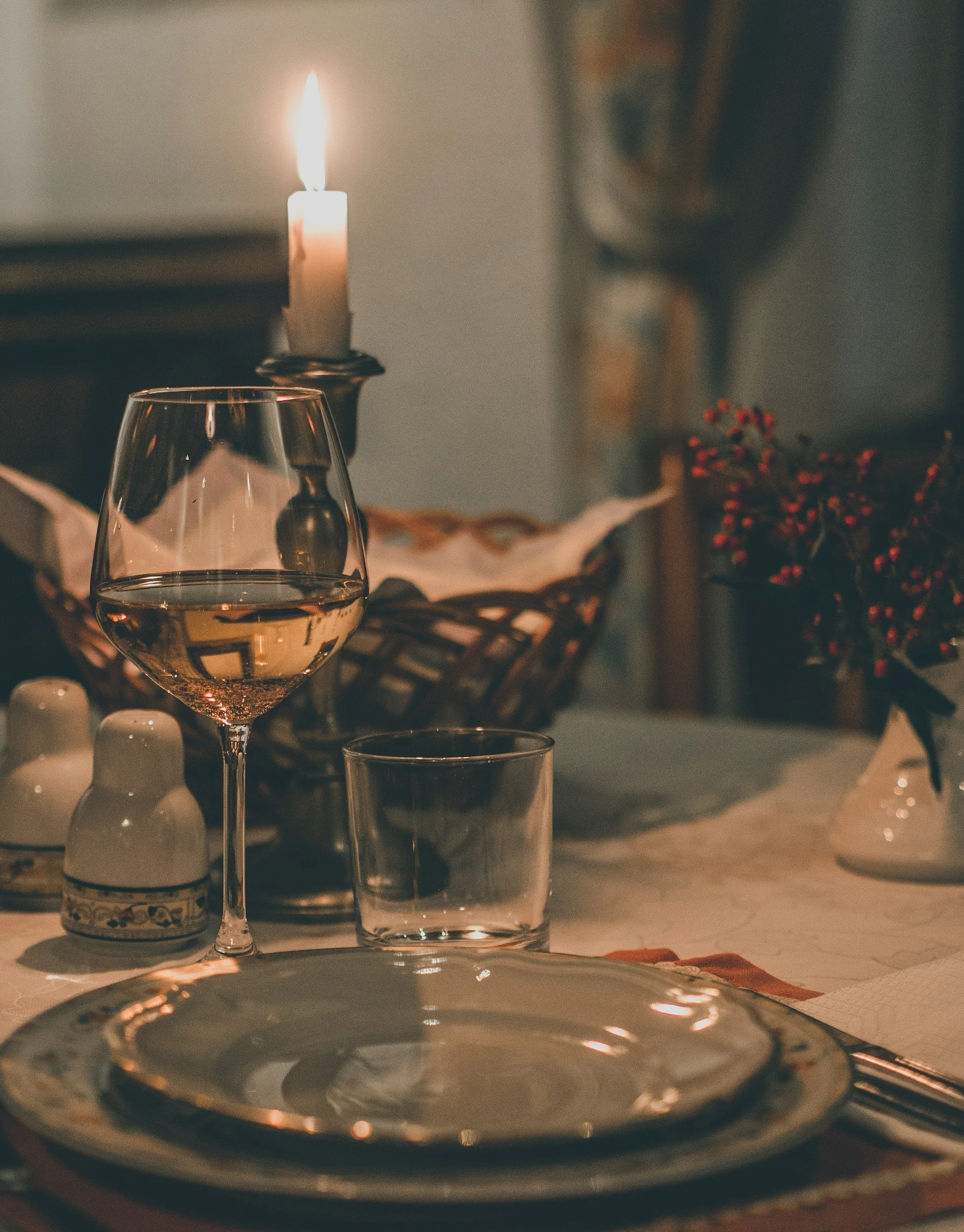 Candlelit table setting with a lit taper candle and glass of wine in a warm, intimate dining atmosphere