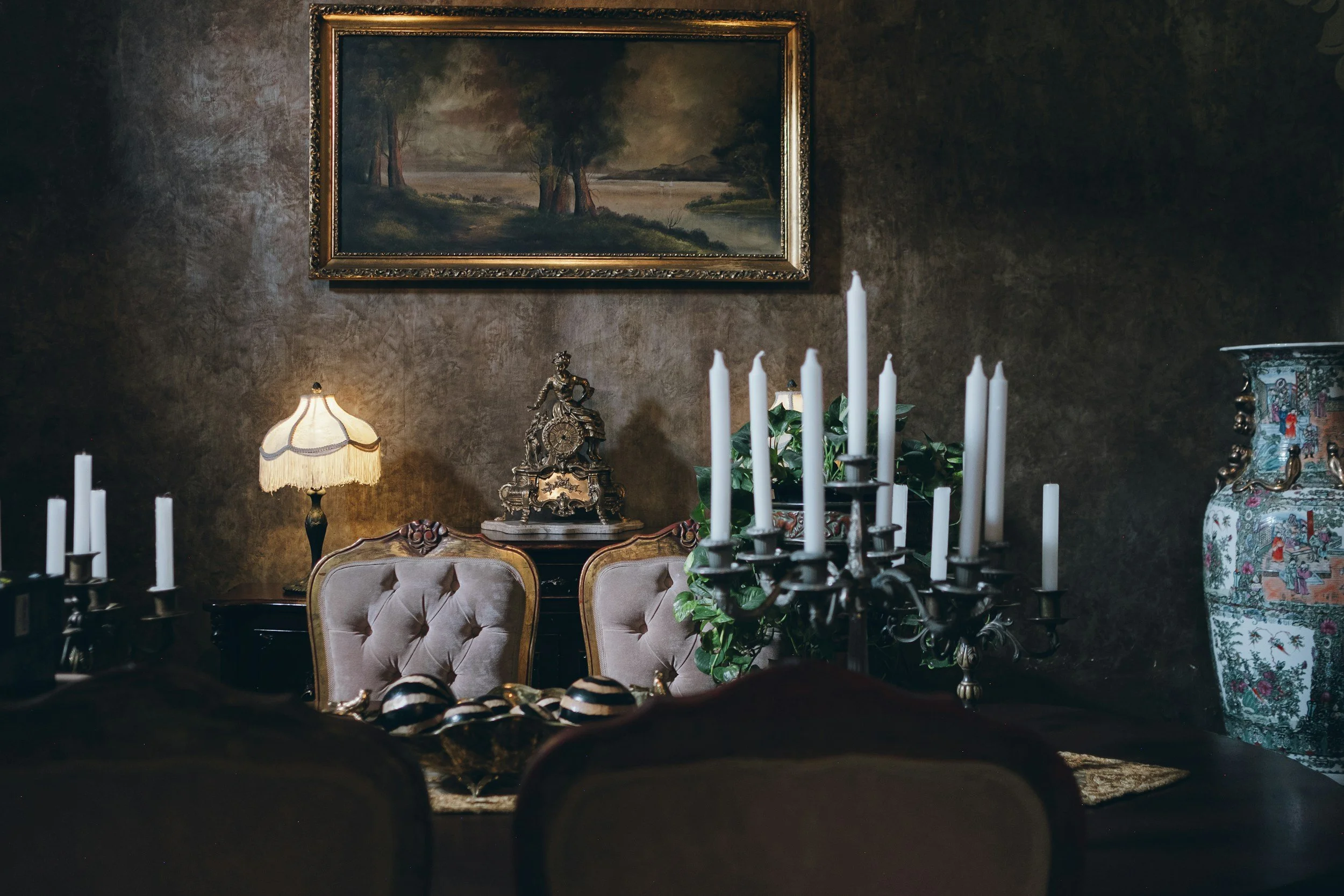 Moody candlelit fine-dining table set with candelabra, framed art, and velvet chairs