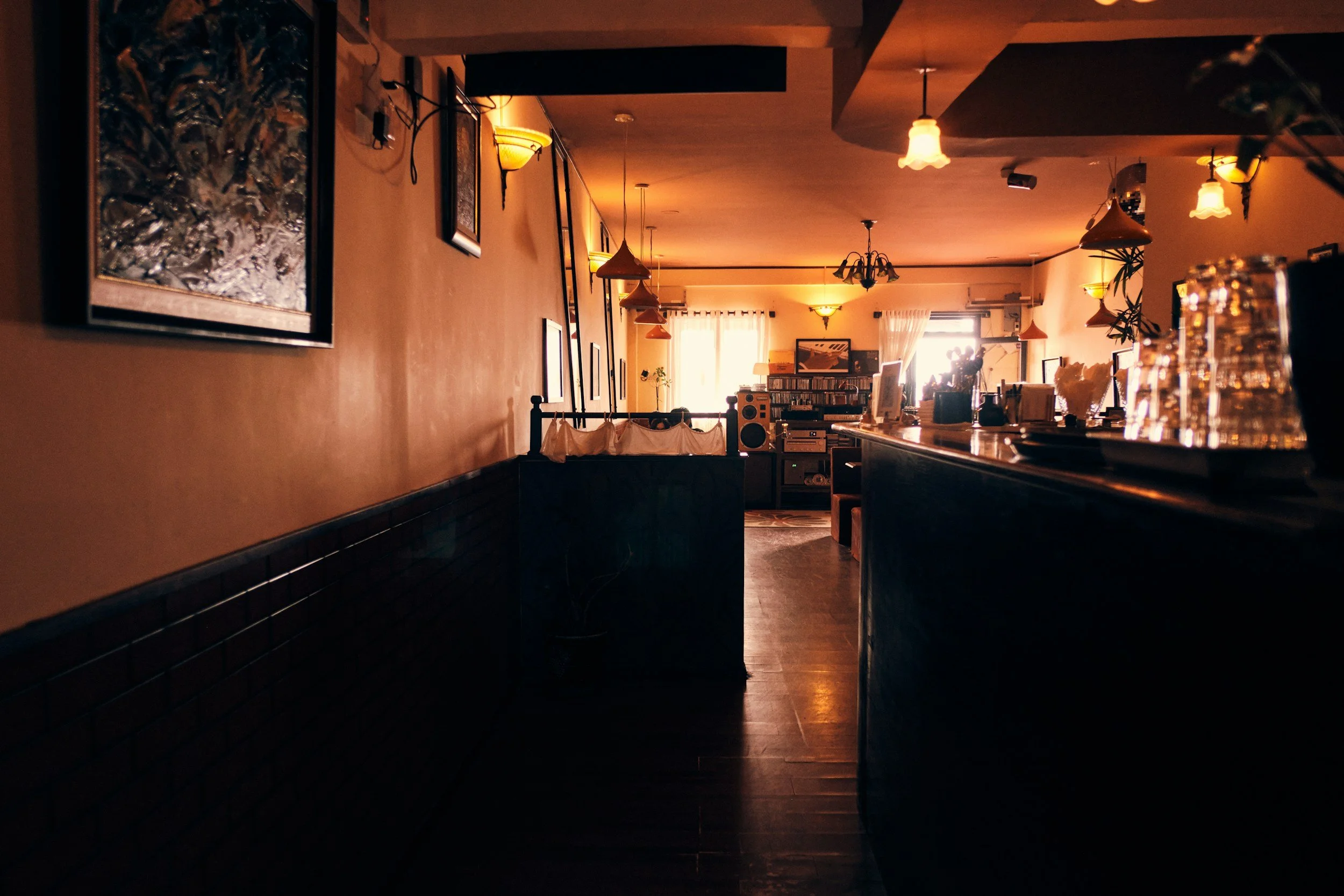 Warm, amber-lit café and bar interior with framed art and a wooden counter, evoking a cozy neighborhood social spot