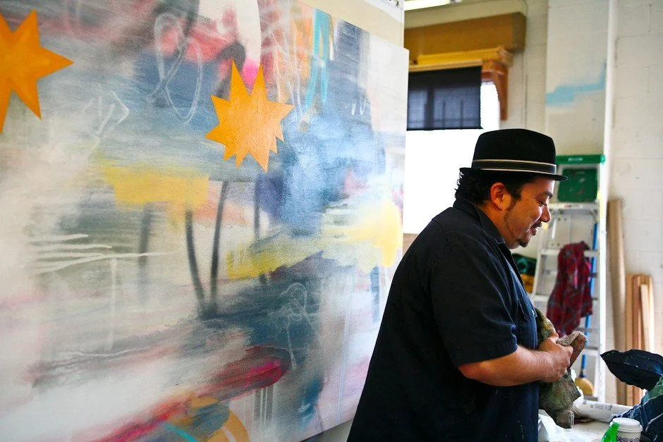 Artist prepares art supplies with his painting behind him