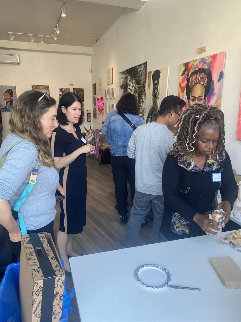 Several people getting drinks and snacks at the snack table at an art gallery event